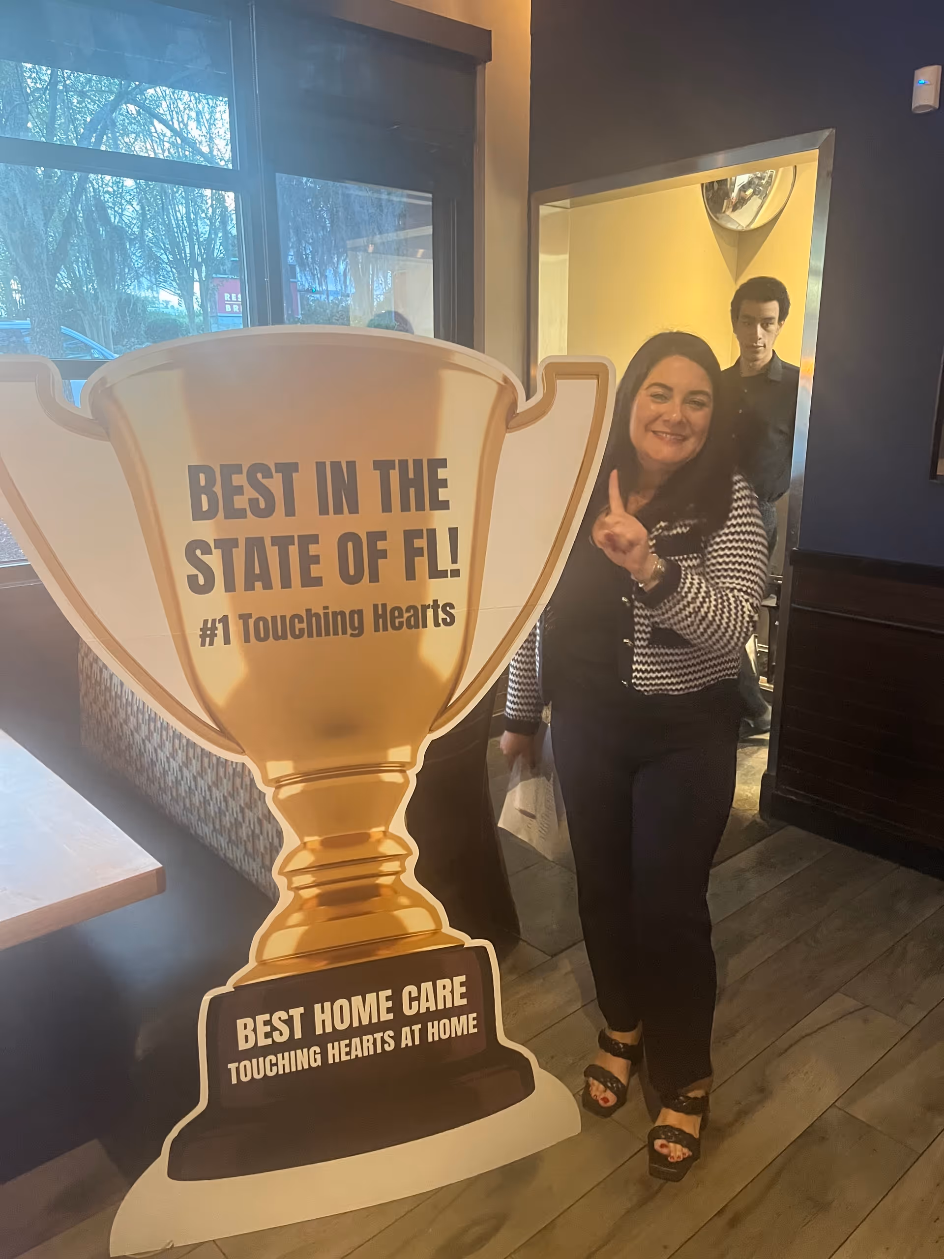 Woman poses beside a large trophy cutout inside a Touching Hearts At Home facility.