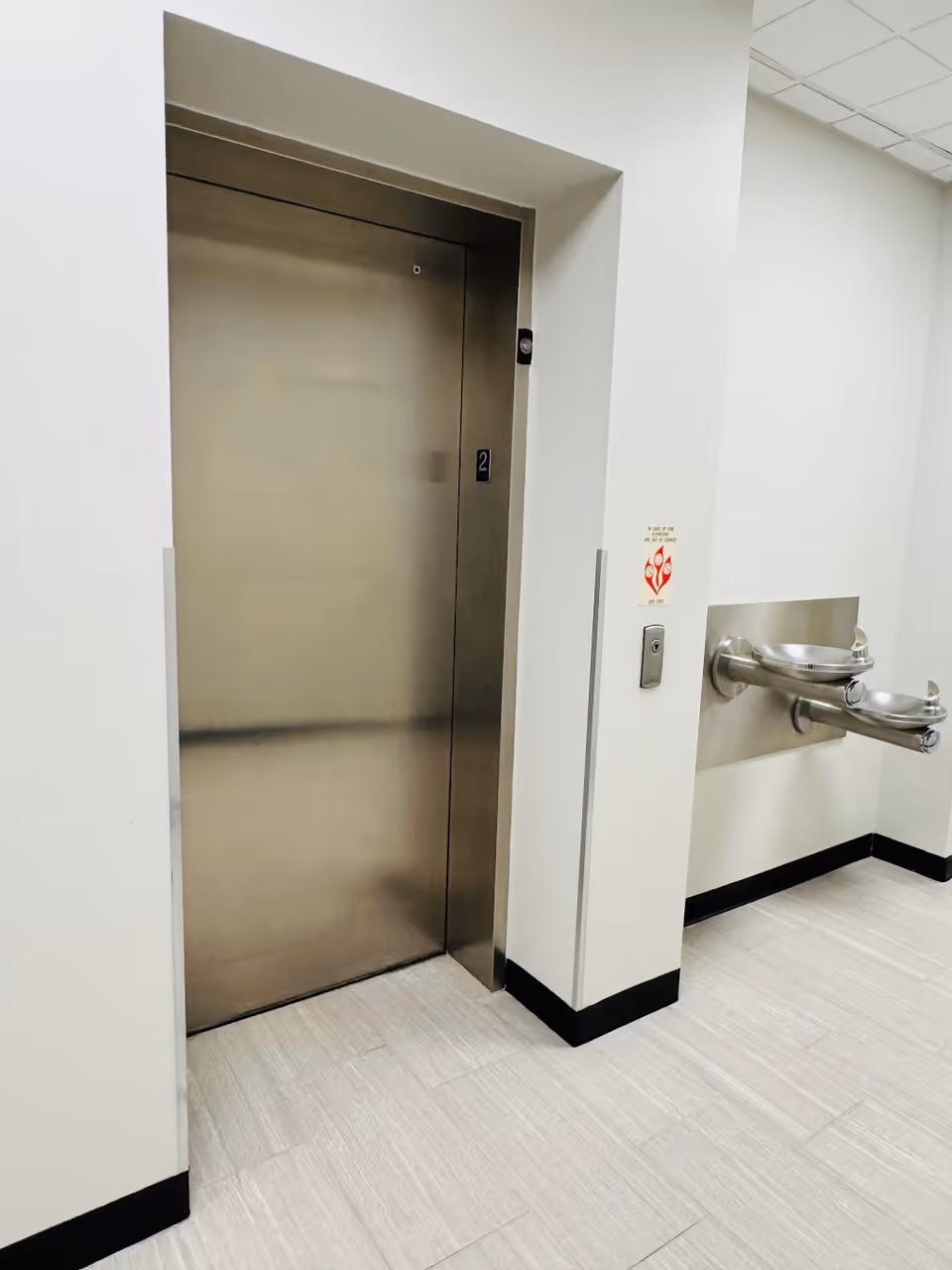 Stainless steel elevator door in a clean, white hallway.