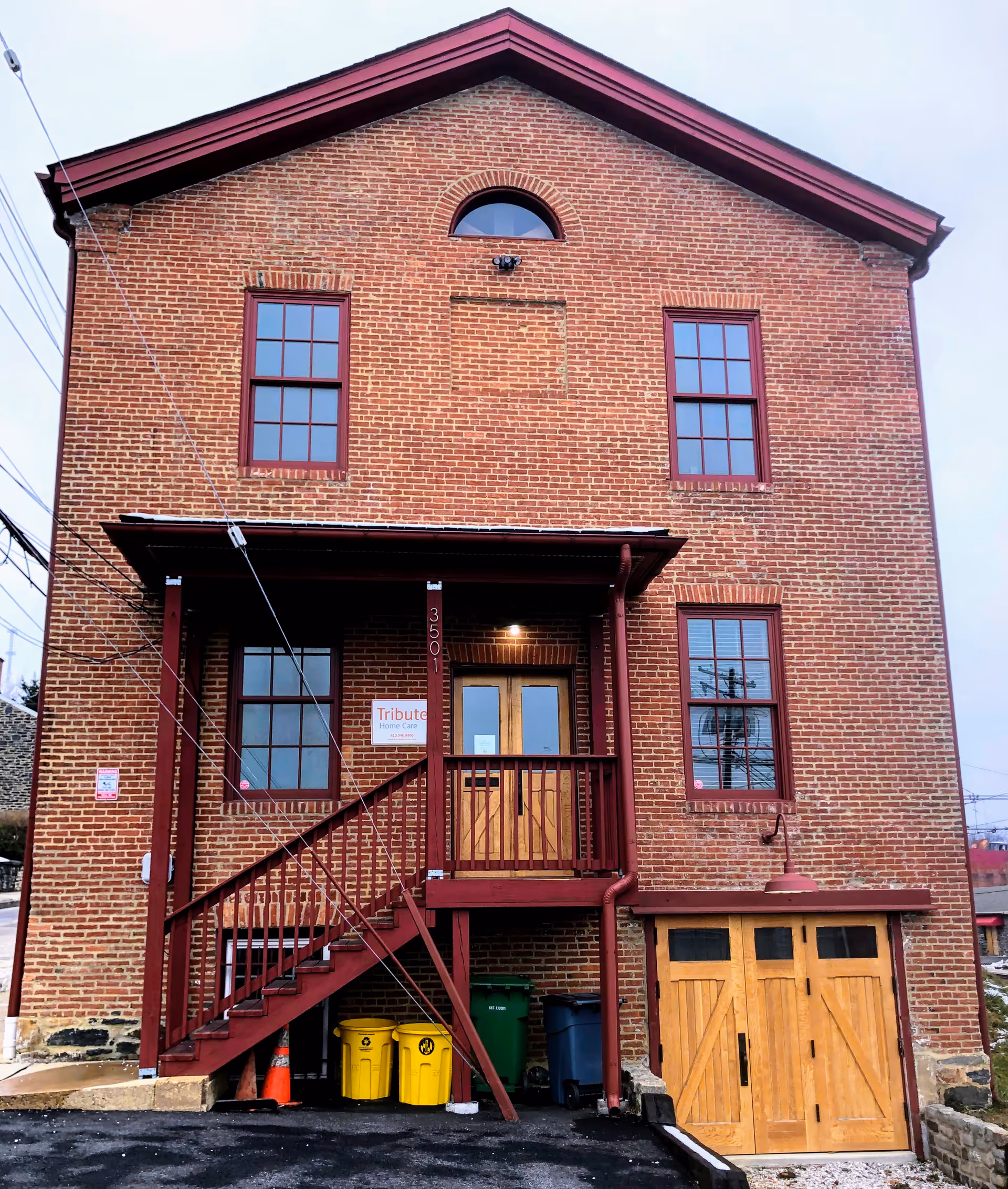 Brick two-story building with red trim, stairs, garage doors, and a Tribute Home Care sign.