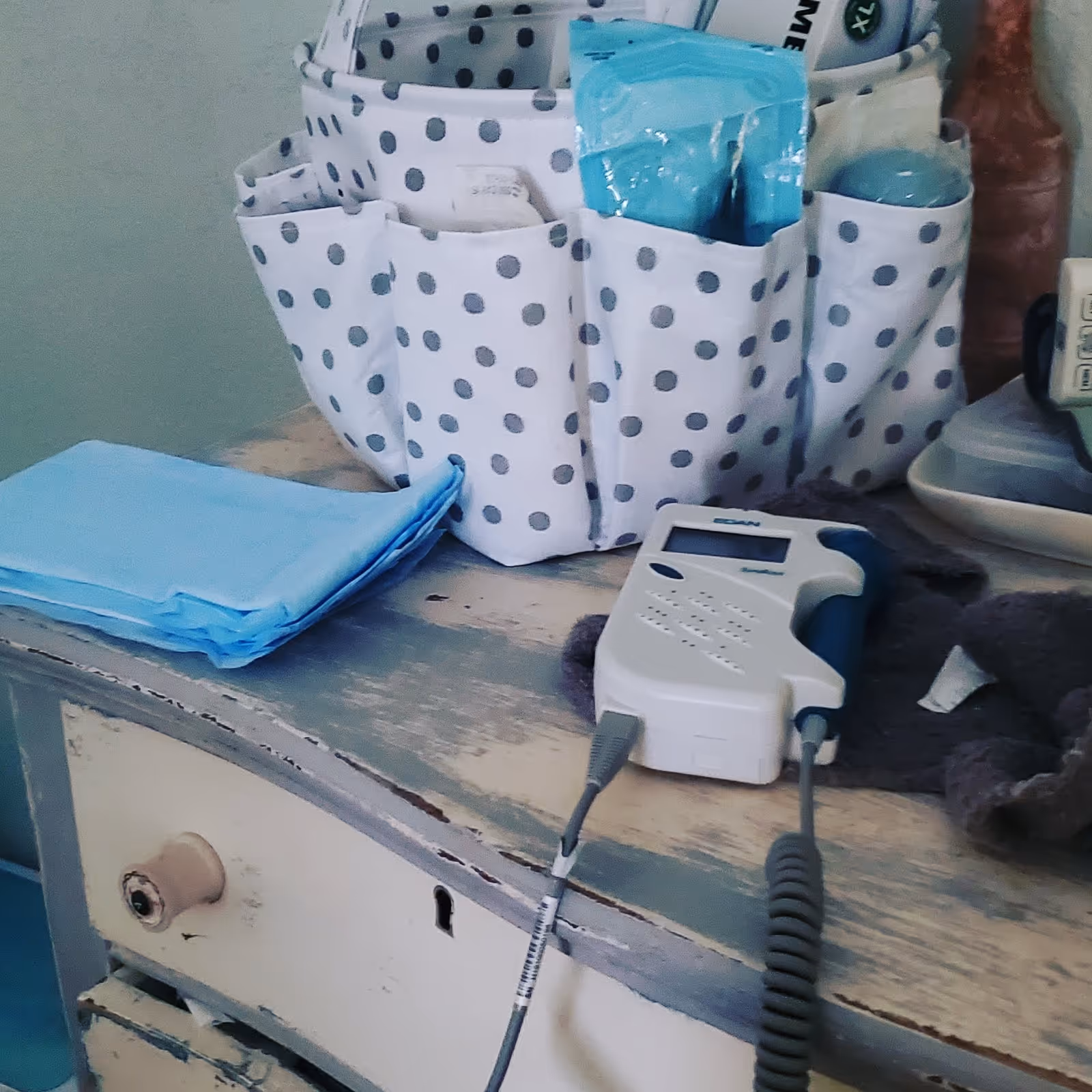 Medical equipment on a weathered dresser, with a polka dot fabric organizer and blue pads.
