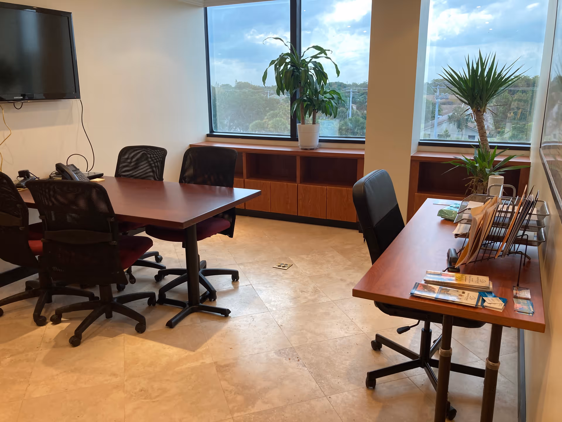 Interior office/meeting area with a wooden table, chairs, and large windows.