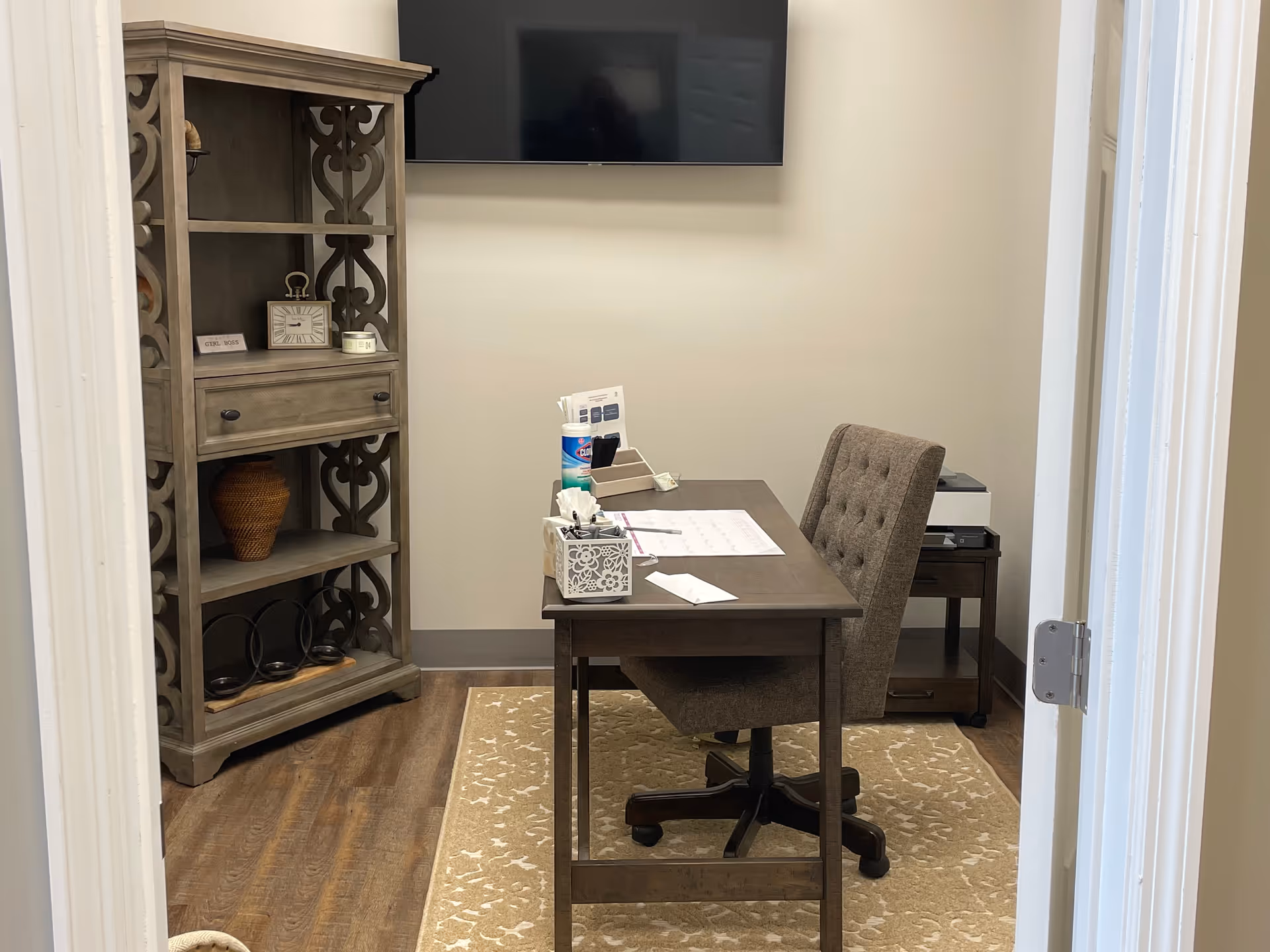 A small office space with a desk, chair, cabinet, and wall-mounted monitor.