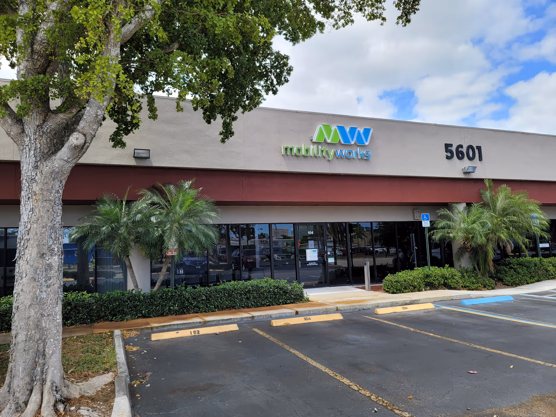Exterior front of MobilityWorks facility with glass entrance, trees, and parking lot.