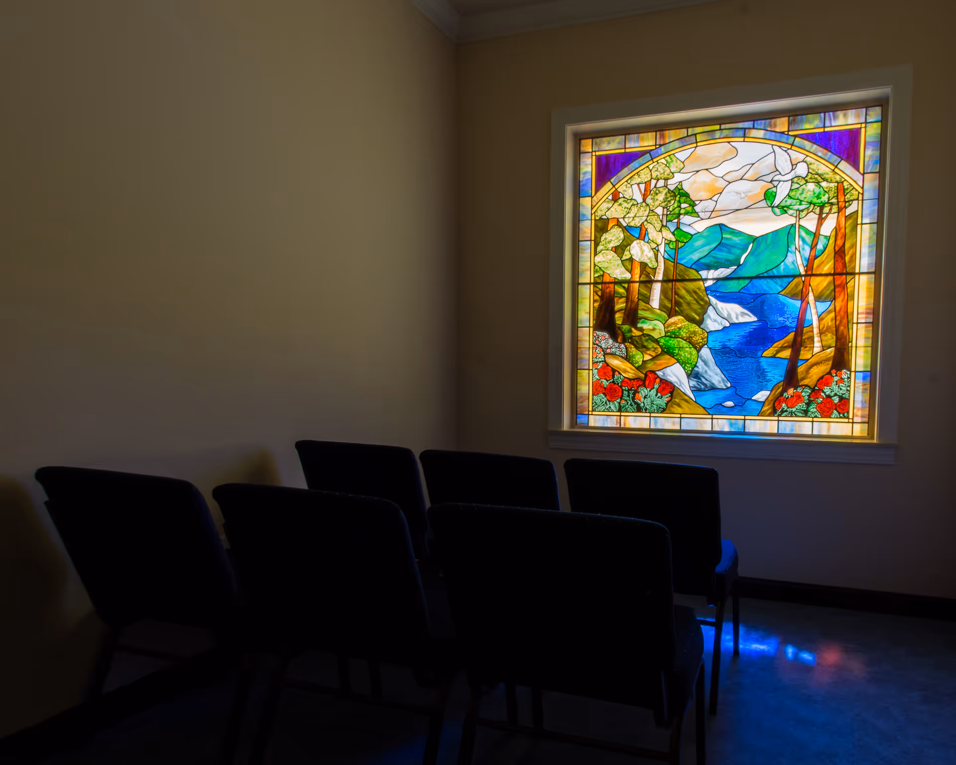Dim interior room with black chairs facing a colorful stained-glass window.