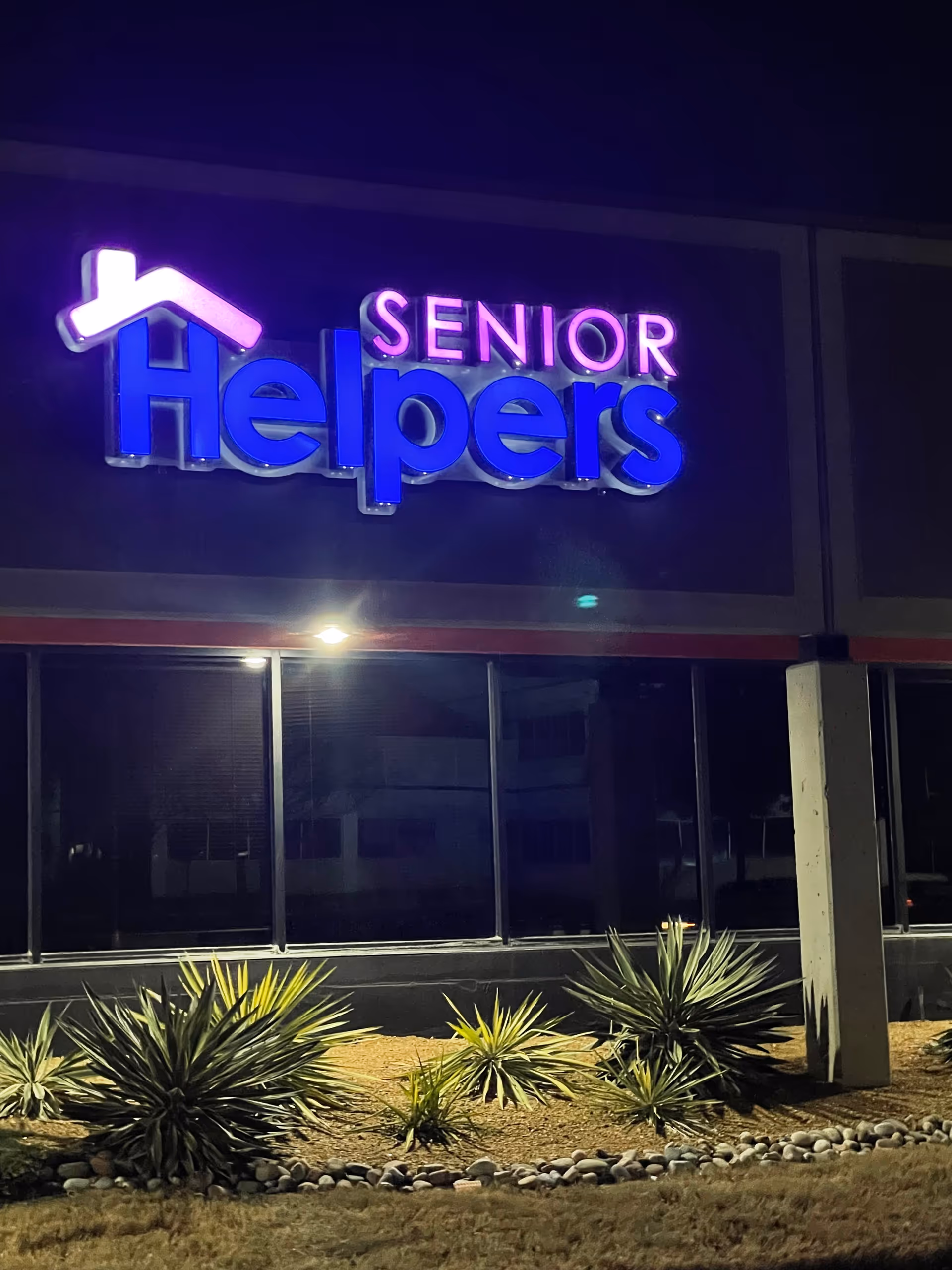 Nighttime exterior of a Senior Helpers facility with a glowing sign.