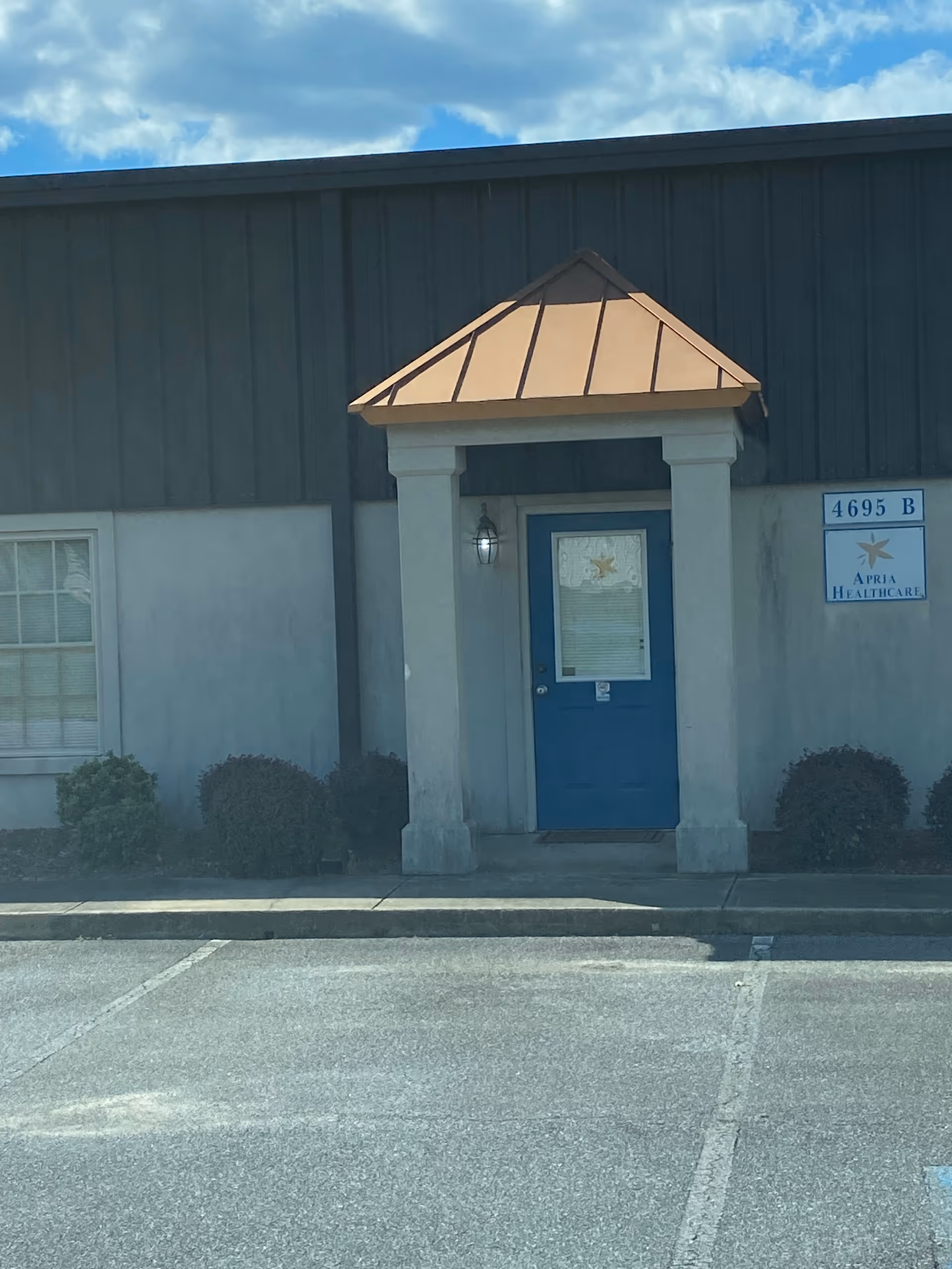 Blue door entrance with copper-colored canopy and Apria Healthcare sign on exterior wall.