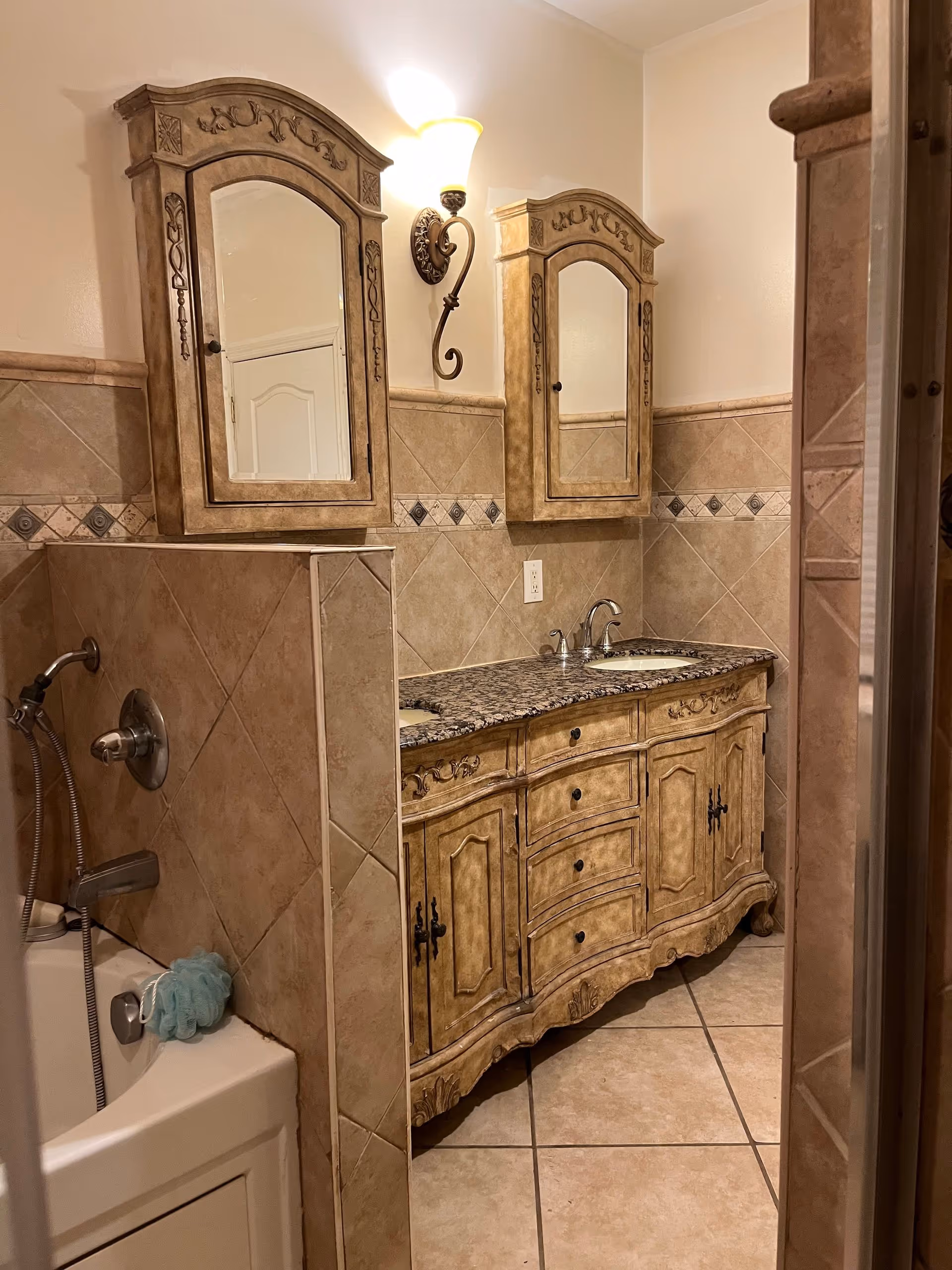 Ornate bathroom vanity with granite countertop, dual mirrors, and tiled walls.