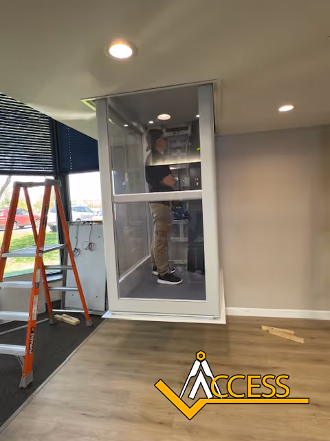 Worker stands inside a glass-walled elevator cab during installation.