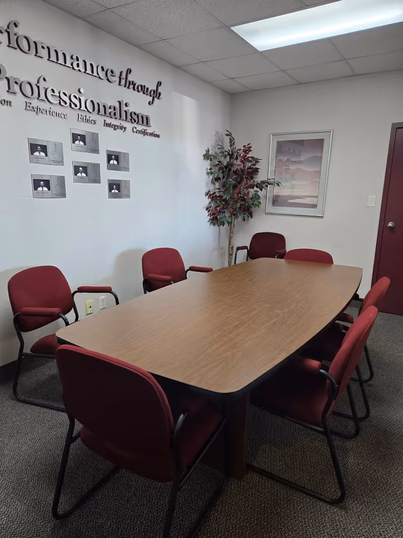 Interior meeting room with a rectangular wooden table and red chairs.