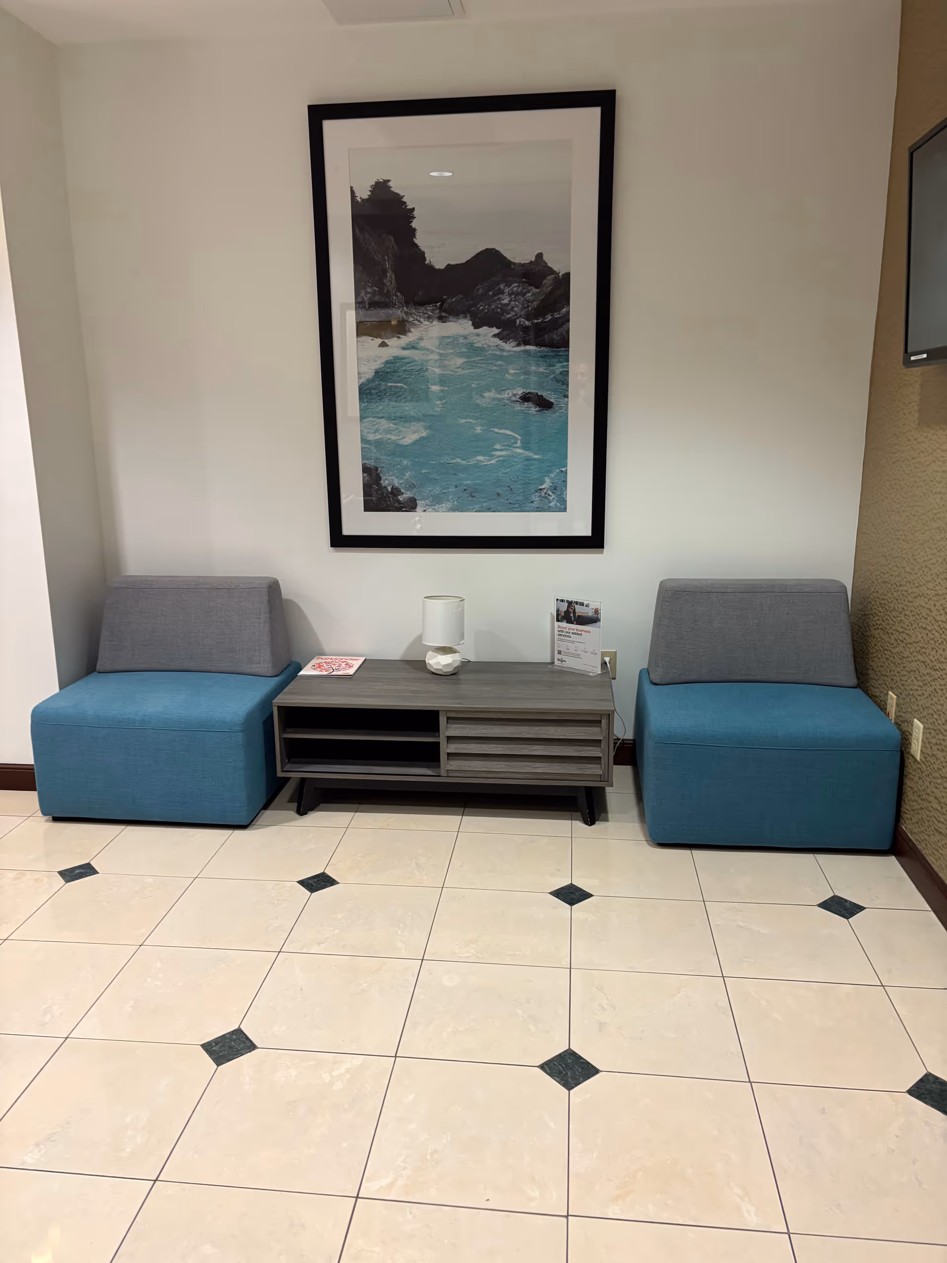 Lobby seating area with two blue ottomans, a console table, and framed wall art.