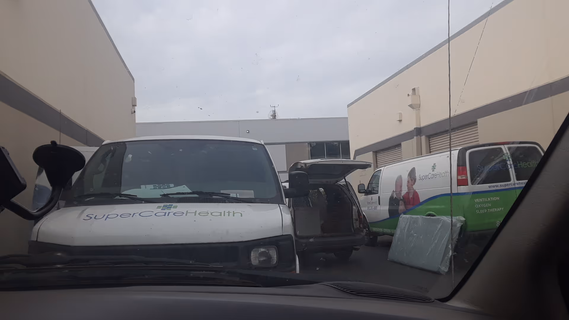 Two SuperCare Health vans parked in a loading area between beige buildings.