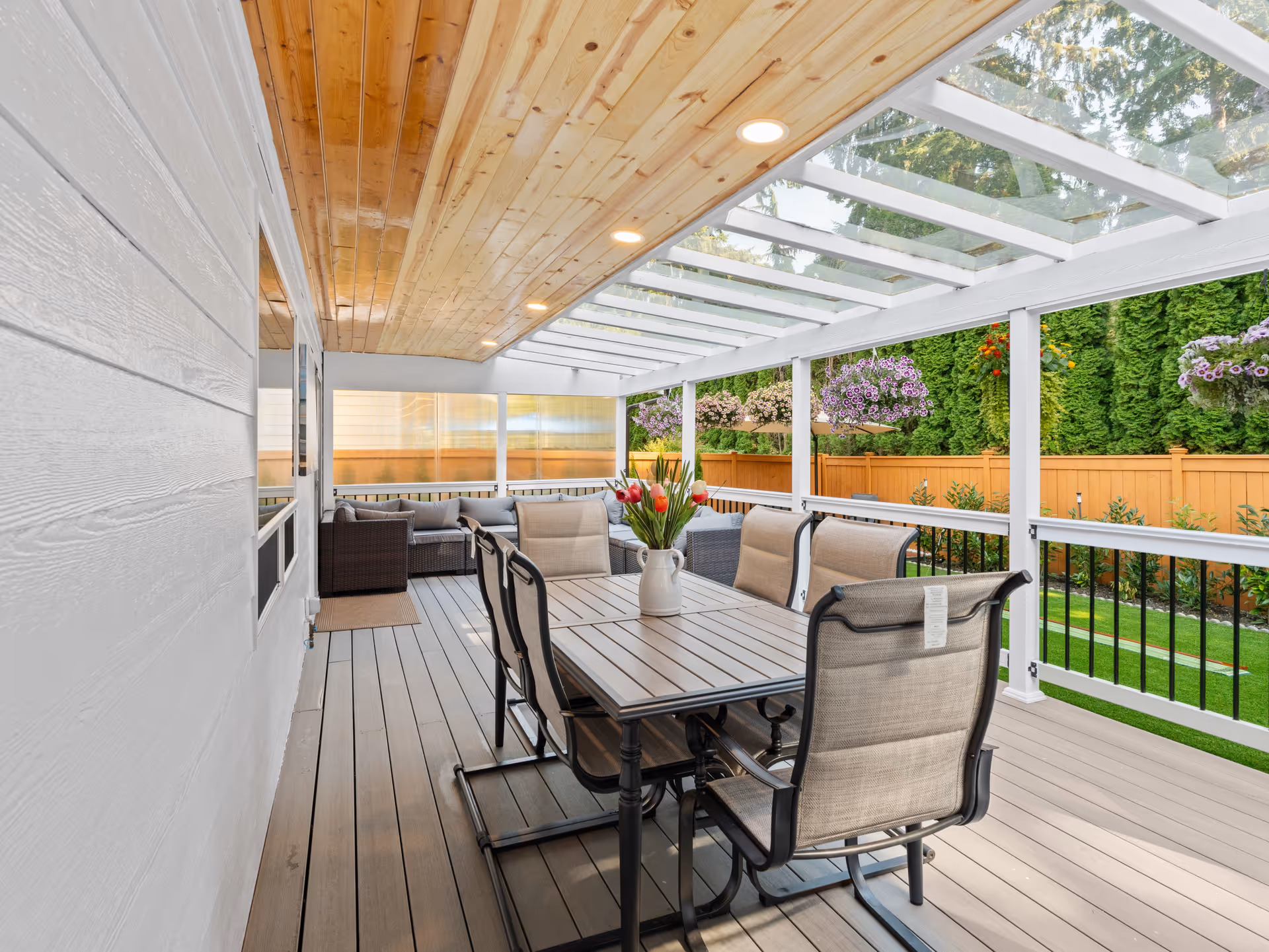 Covered outdoor patio with a large dining table, cushioned chairs, and surrounding greenery.