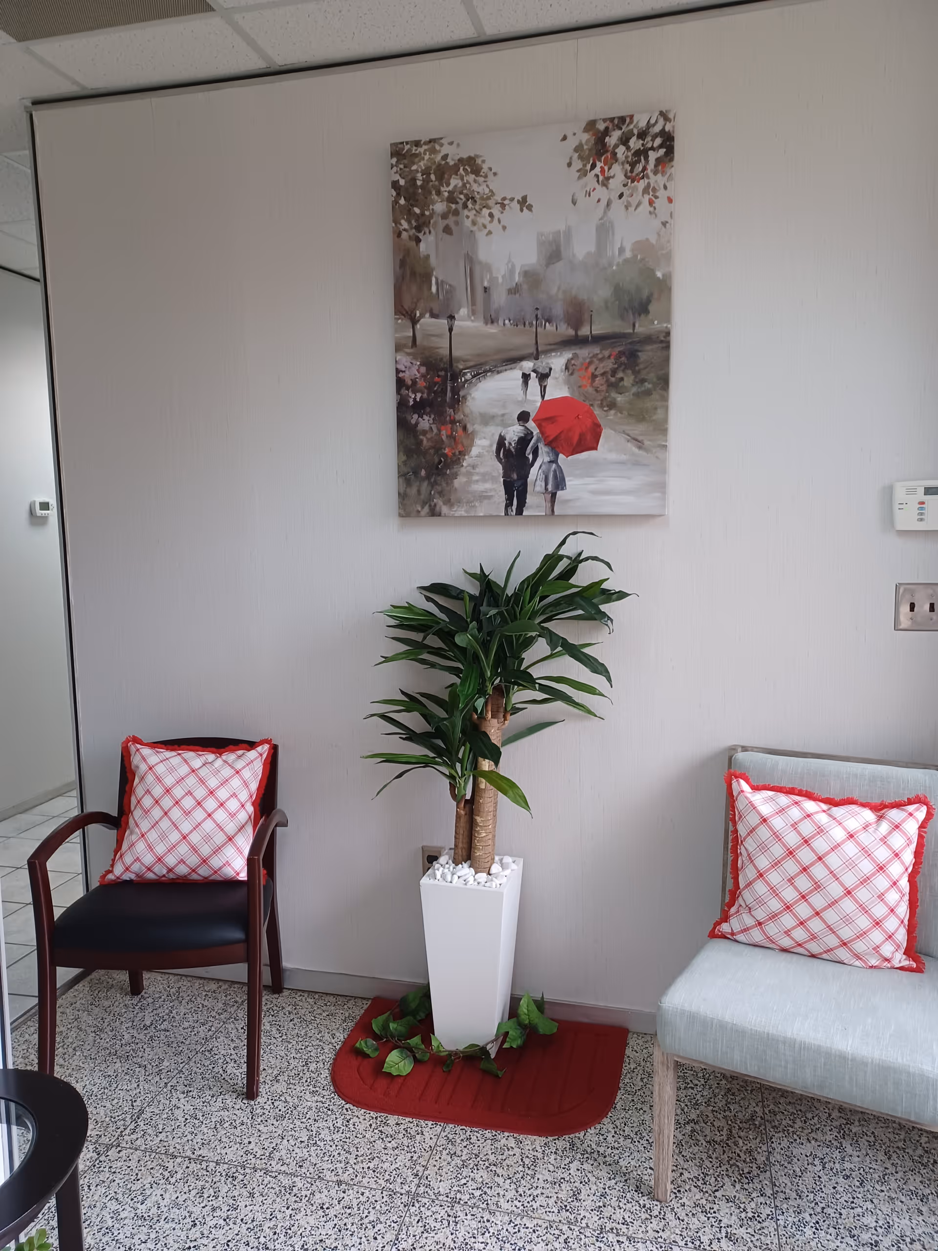Indoor seating area with two chairs, a potted plant, and a wall painting.