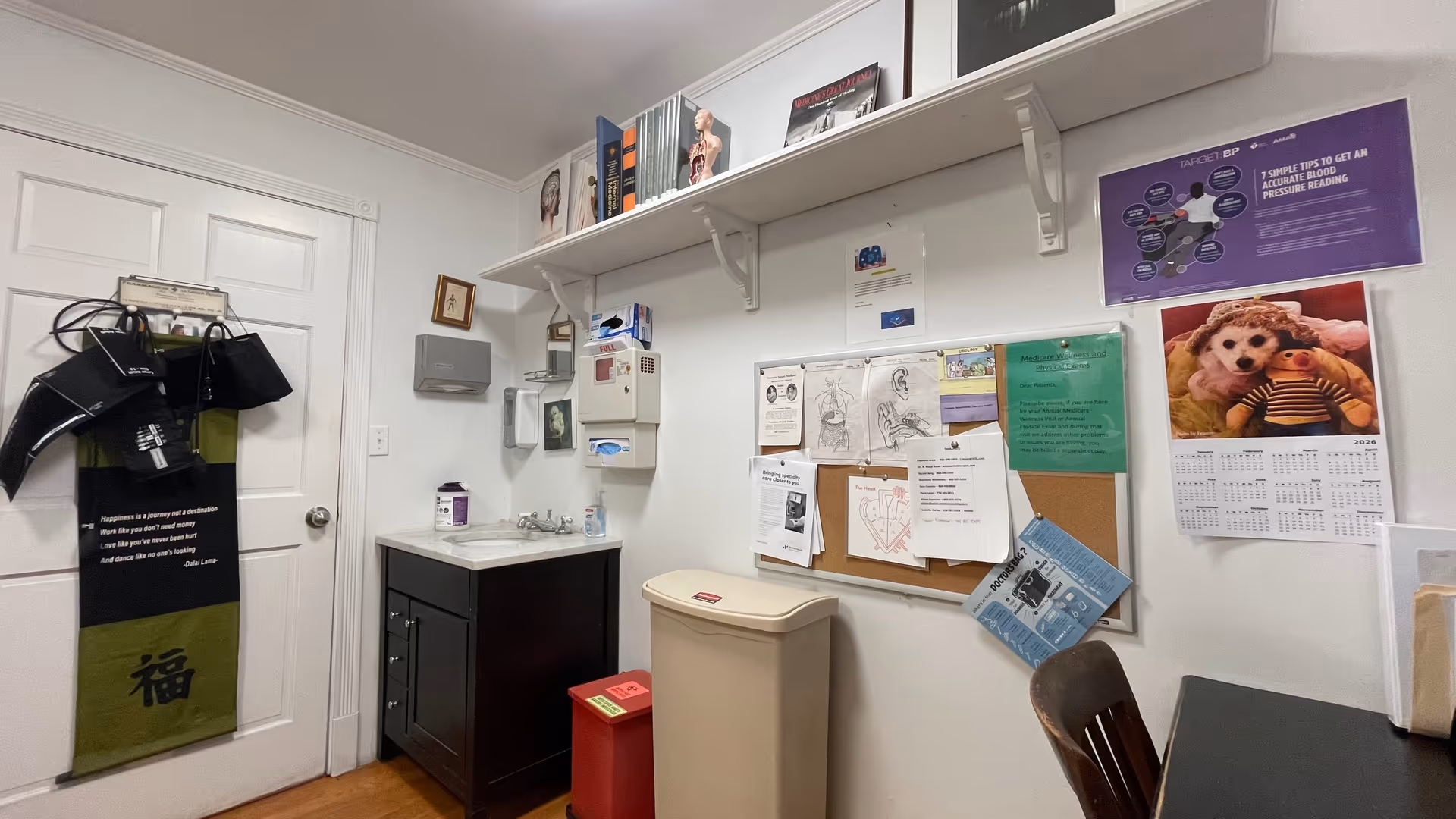 Small staff utility room with sink, cabinets, bulletin board, shelves, and a calendar.