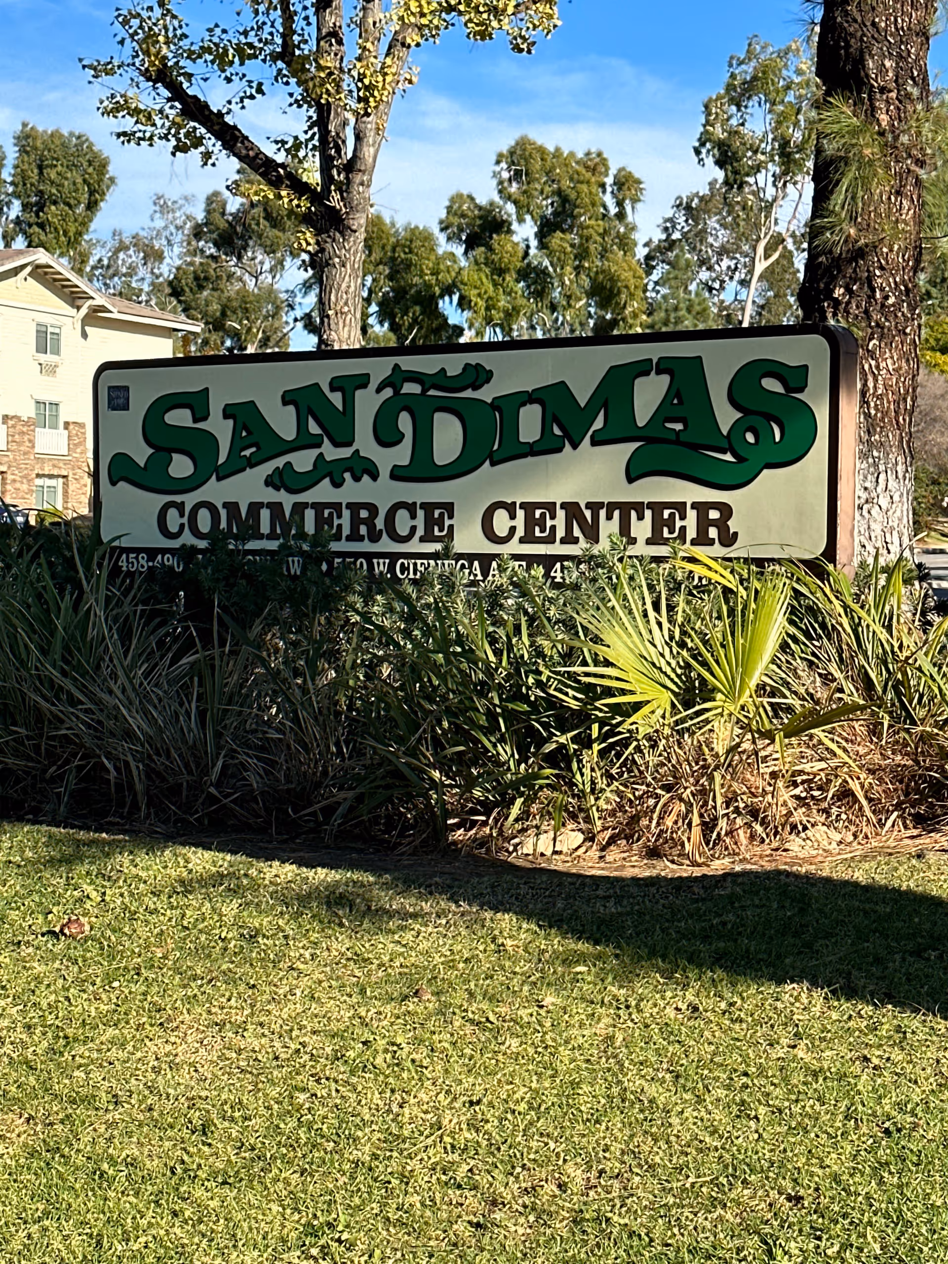 Outdoor sign reading San Dimas Commerce Center with plants and trees around.