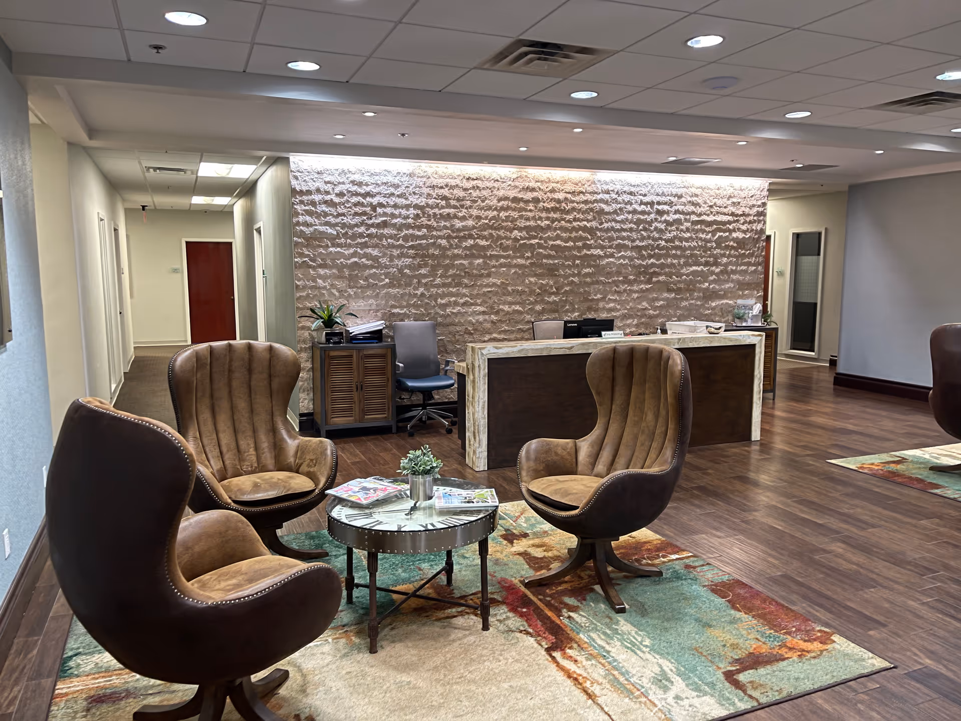Modern senior living lobby with brown lounge chairs, a round glass table, and a reception desk.