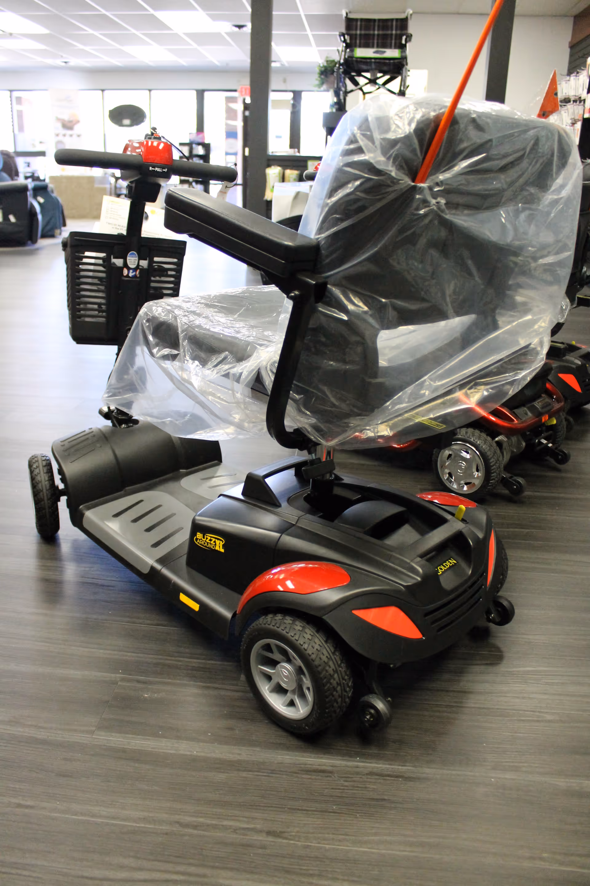 Electric mobility scooter with plastic cover in a store showroom, medical equipment visible.