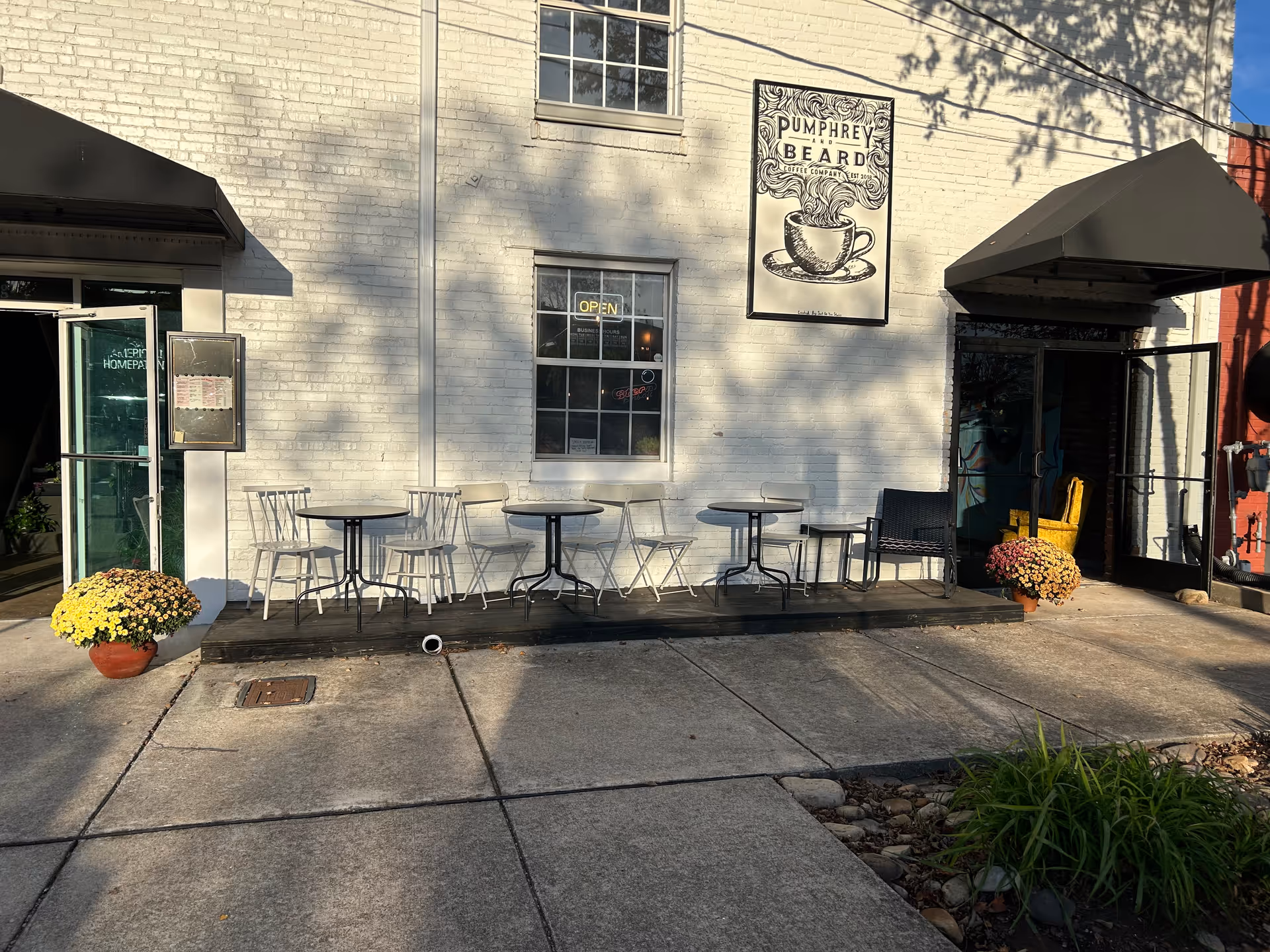Exterior view of a white brick building with outdoor seating and potted flowers.