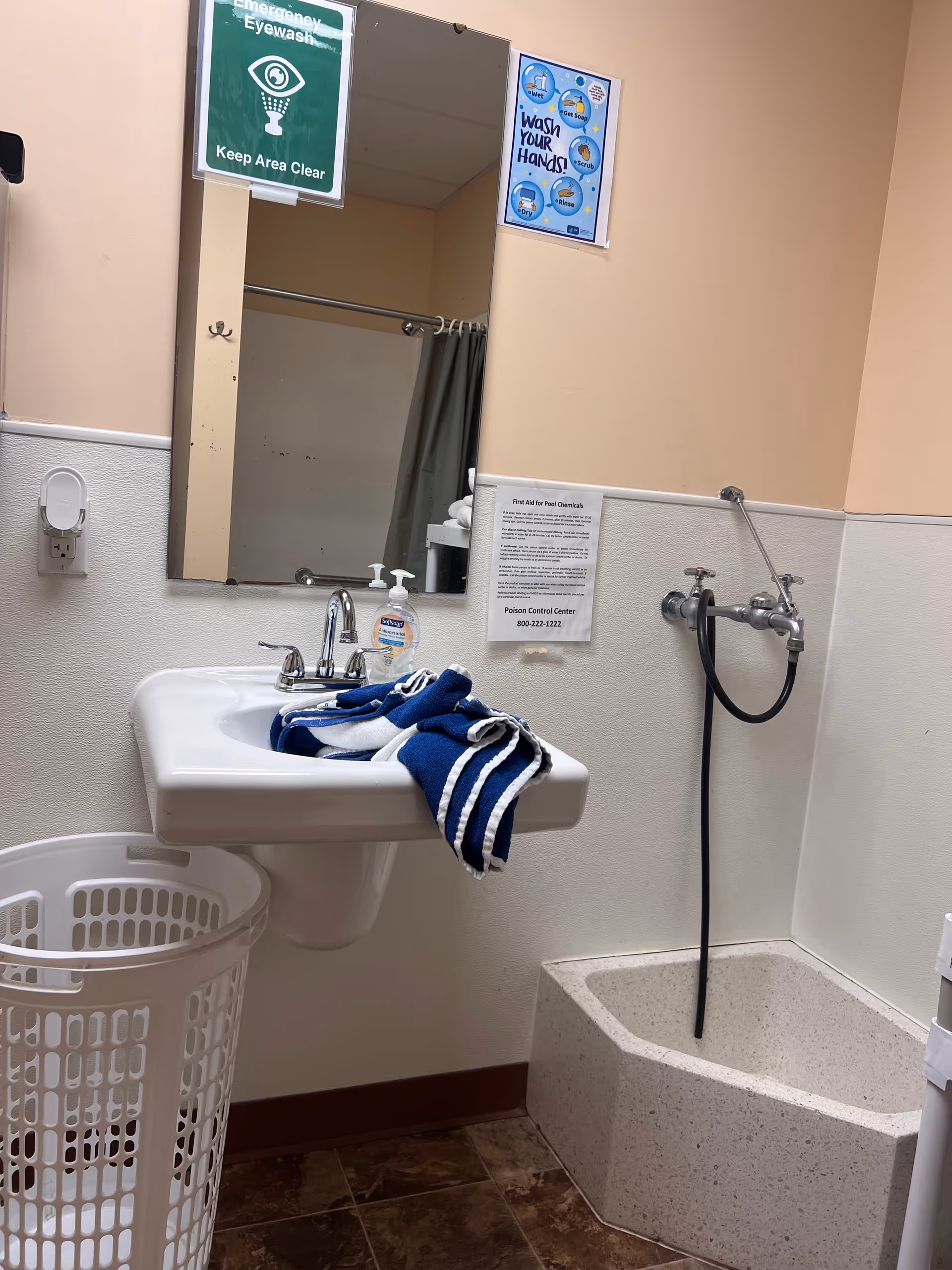 Facility bathroom with sink, mirror, towels, laundry basket, shower, and safety signs.