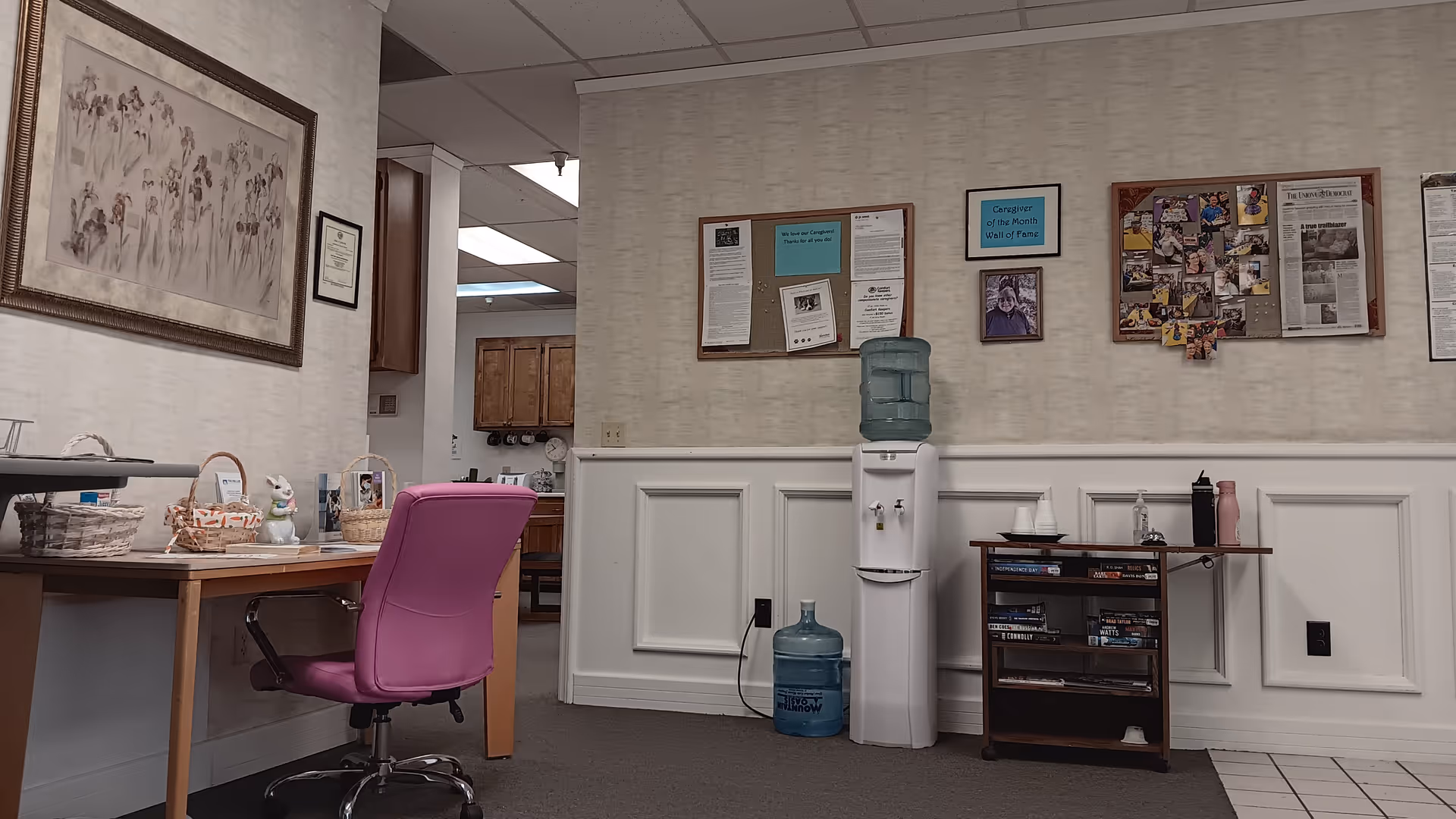 A common area with a pink office chair, water cooler, bulletin boards, and a desk.