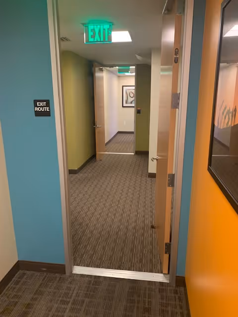 Indoor hallway of a senior living facility with doors, carpet, and exit signs.
