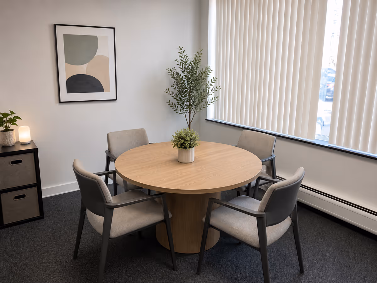 Round wooden dining table with five upholstered chairs in a bright, minimalist room.