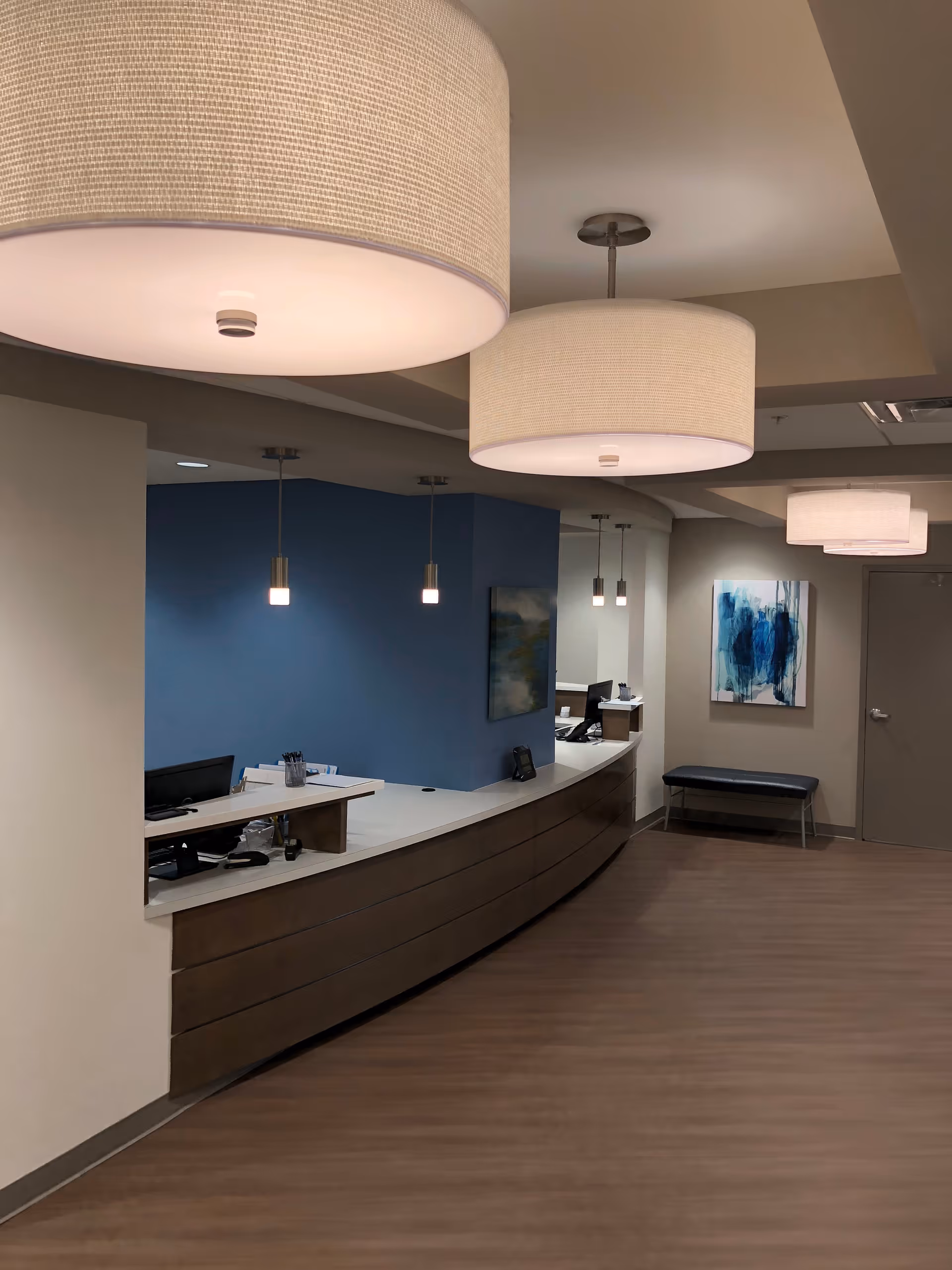 Reception area with curved wooden desk, blue accent wall, and hanging pendant lights.