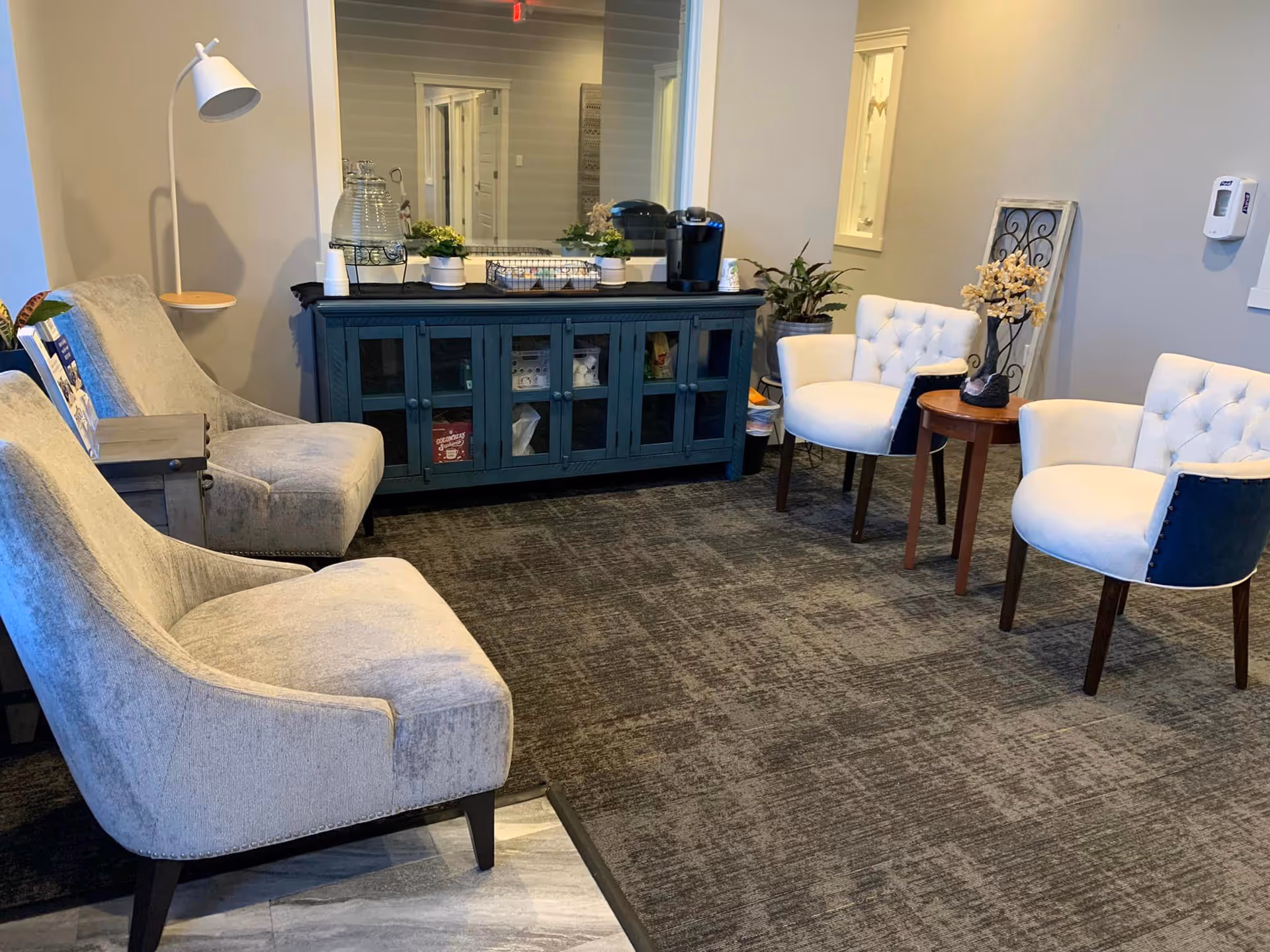 A cozy waiting area with tufted chairs, a dark green cabinet, and plants.