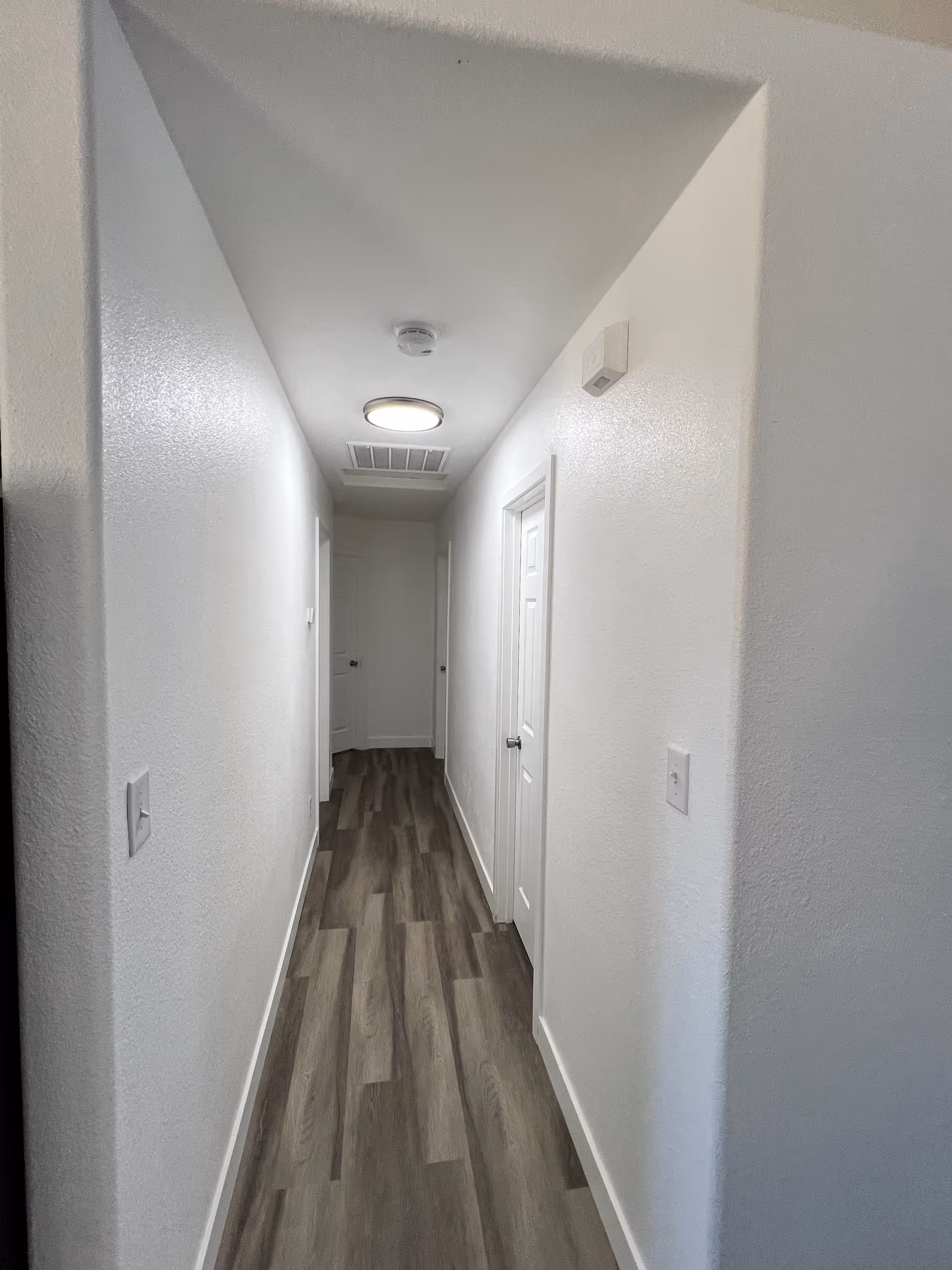 White hallway with doors on both sides and wood-patterned flooring in a senior living facility.