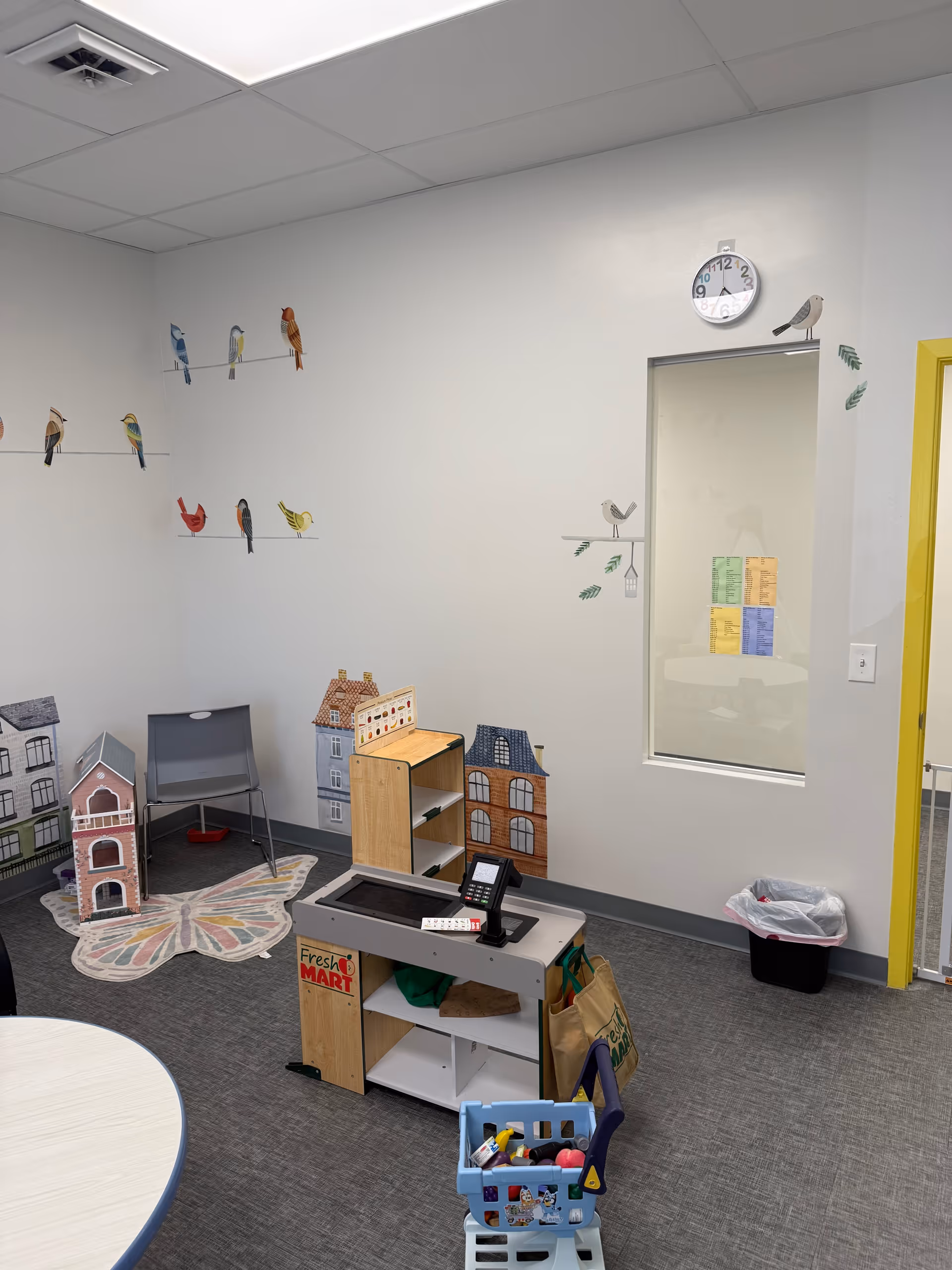 Indoor therapy playroom with toy houses, shelves, and bird decals on light walls.