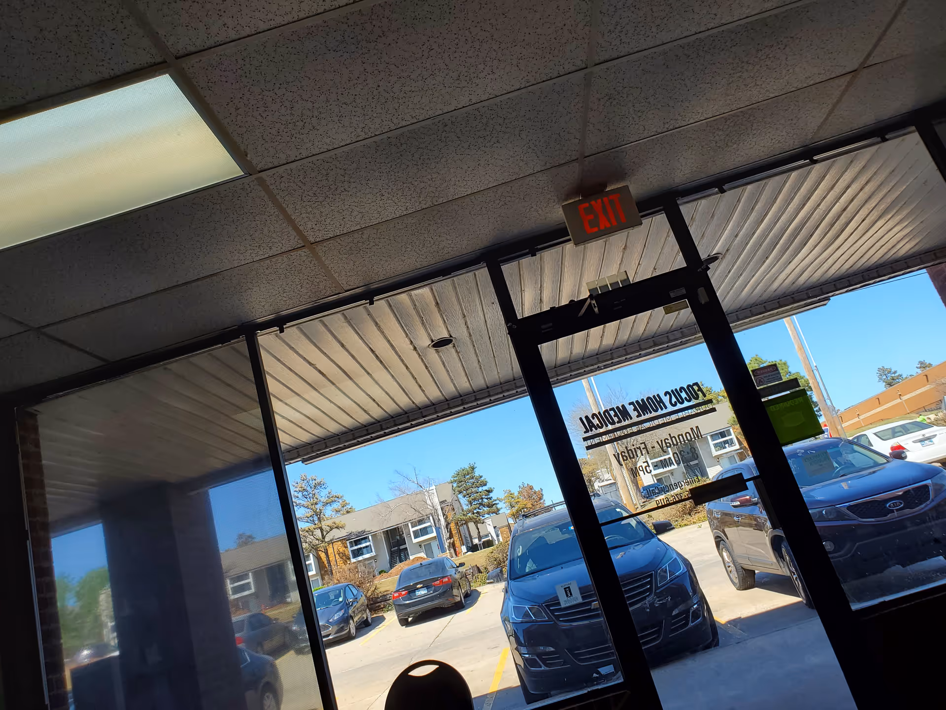 Interior entrance with glass doors, EXIT sign, and view of parked cars outside.