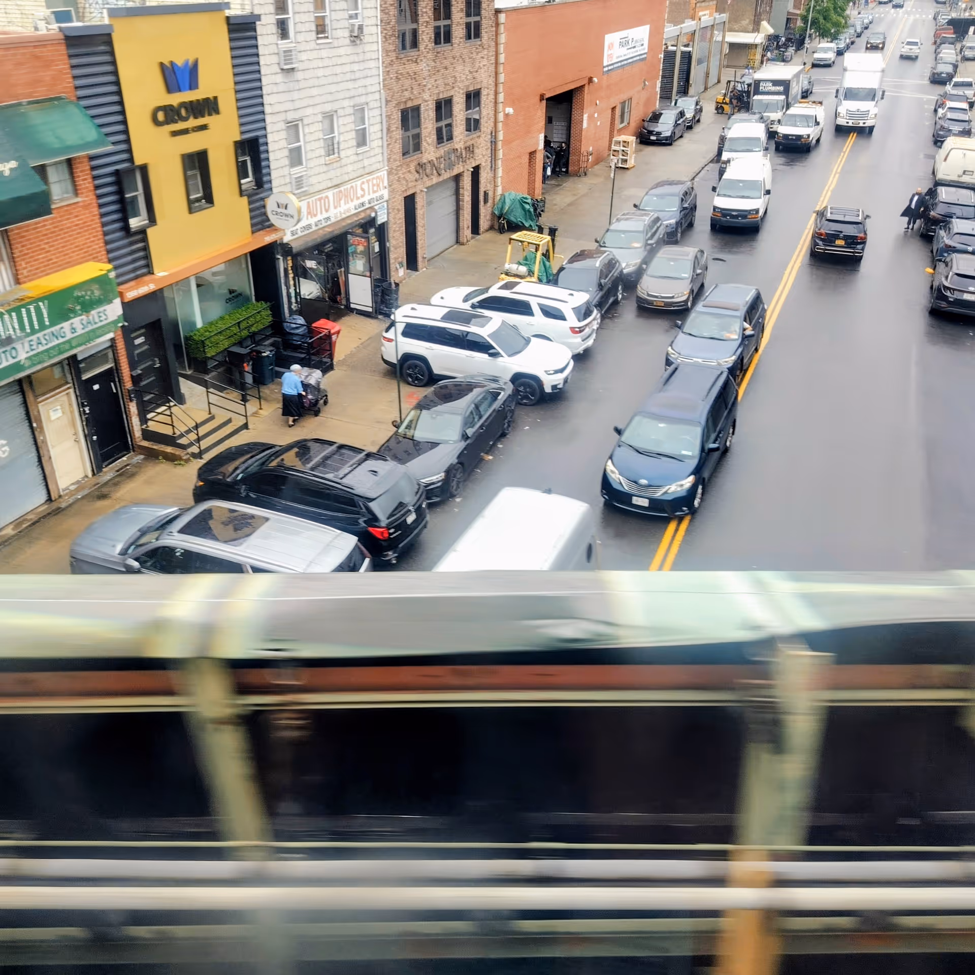 A city street view with parked cars, storefronts, and a Crown sign on a yellow building.