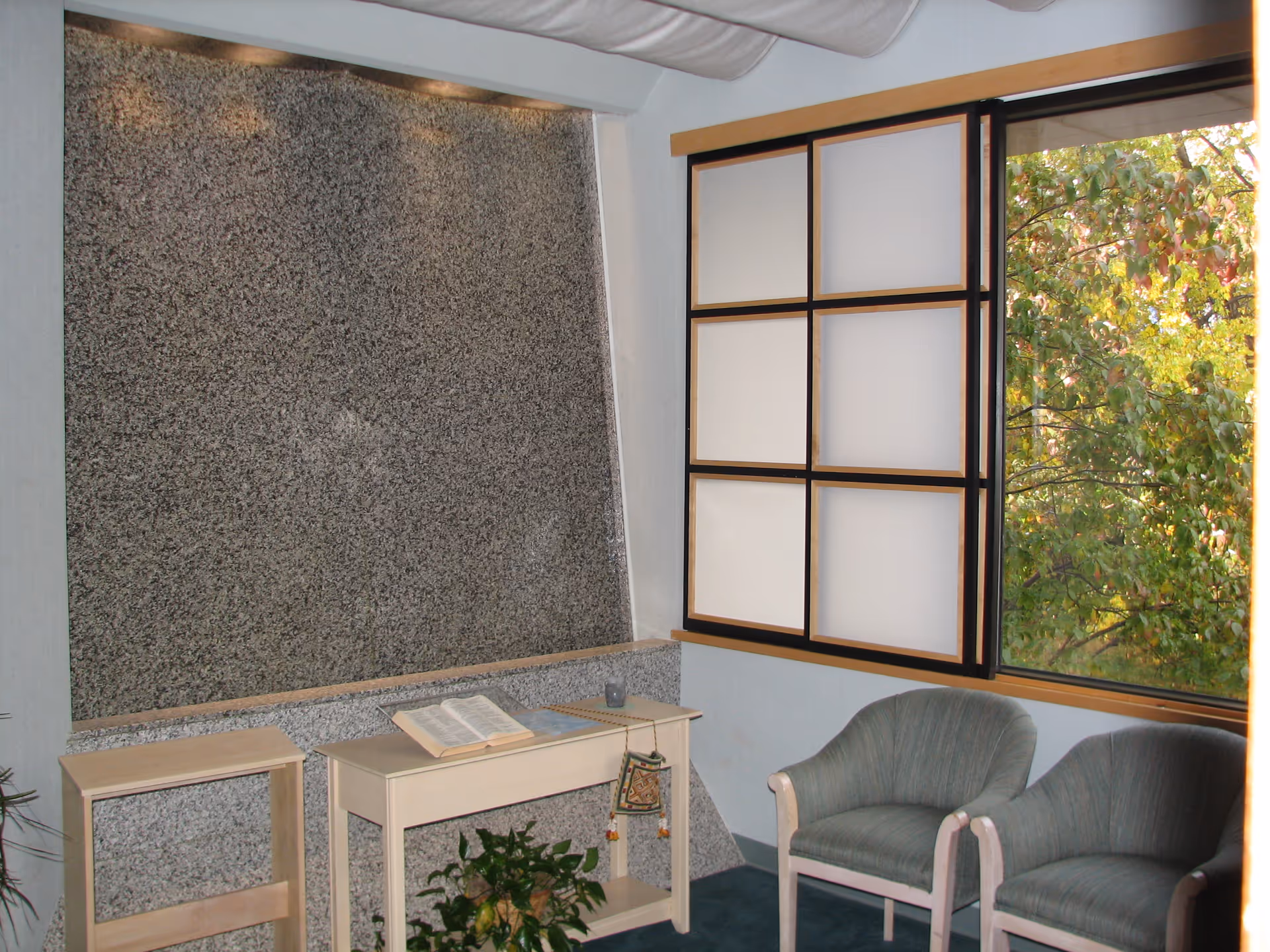 A small interior room with a speckled wall, frosted window, two chairs, and a desk.
