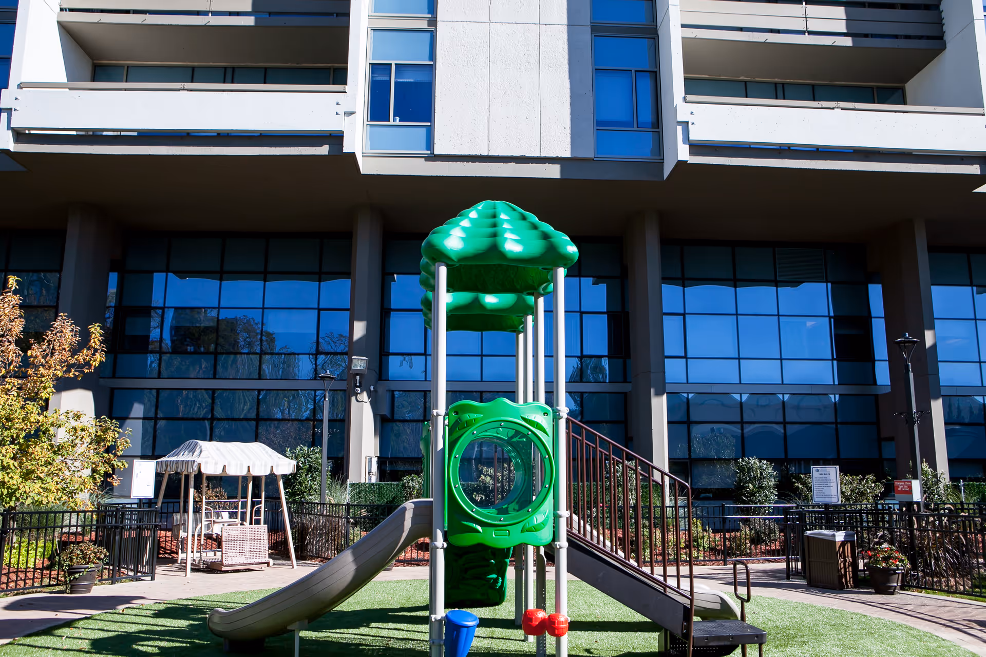 Modern building exterior with glass windows and a green outdoor playground.