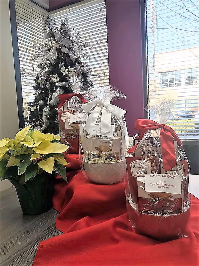 Decorated holiday area with a Christmas tree, gift baskets, and poinsettia on a table near windows.