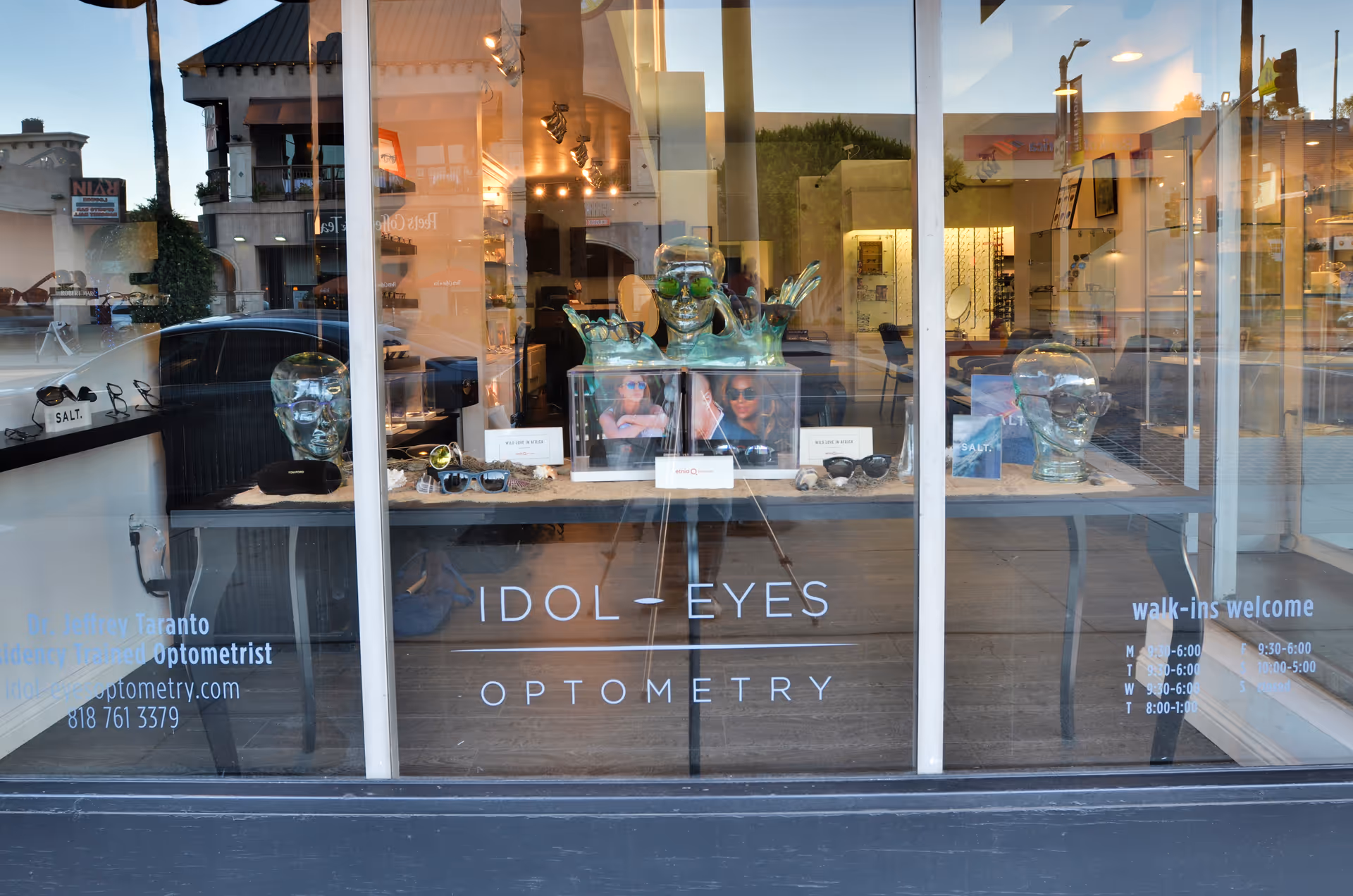 Storefront window display at Idol Eyes Optometry featuring glass busts and sunglasses.