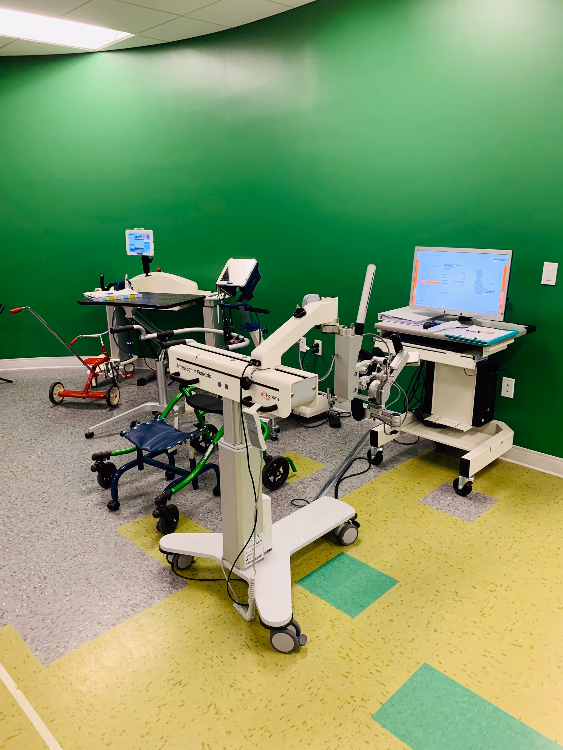 Green-walled therapy room with medical equipment and wheeled rehabilitation devices.