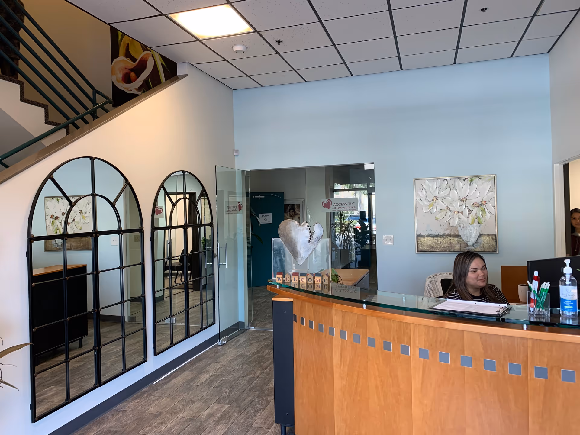 Bright lobby with curved staircase, arched glass panels, and a receptionist at the desk.
