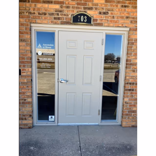 Brick building exterior with central white door, glass side panels, and 703 sign.