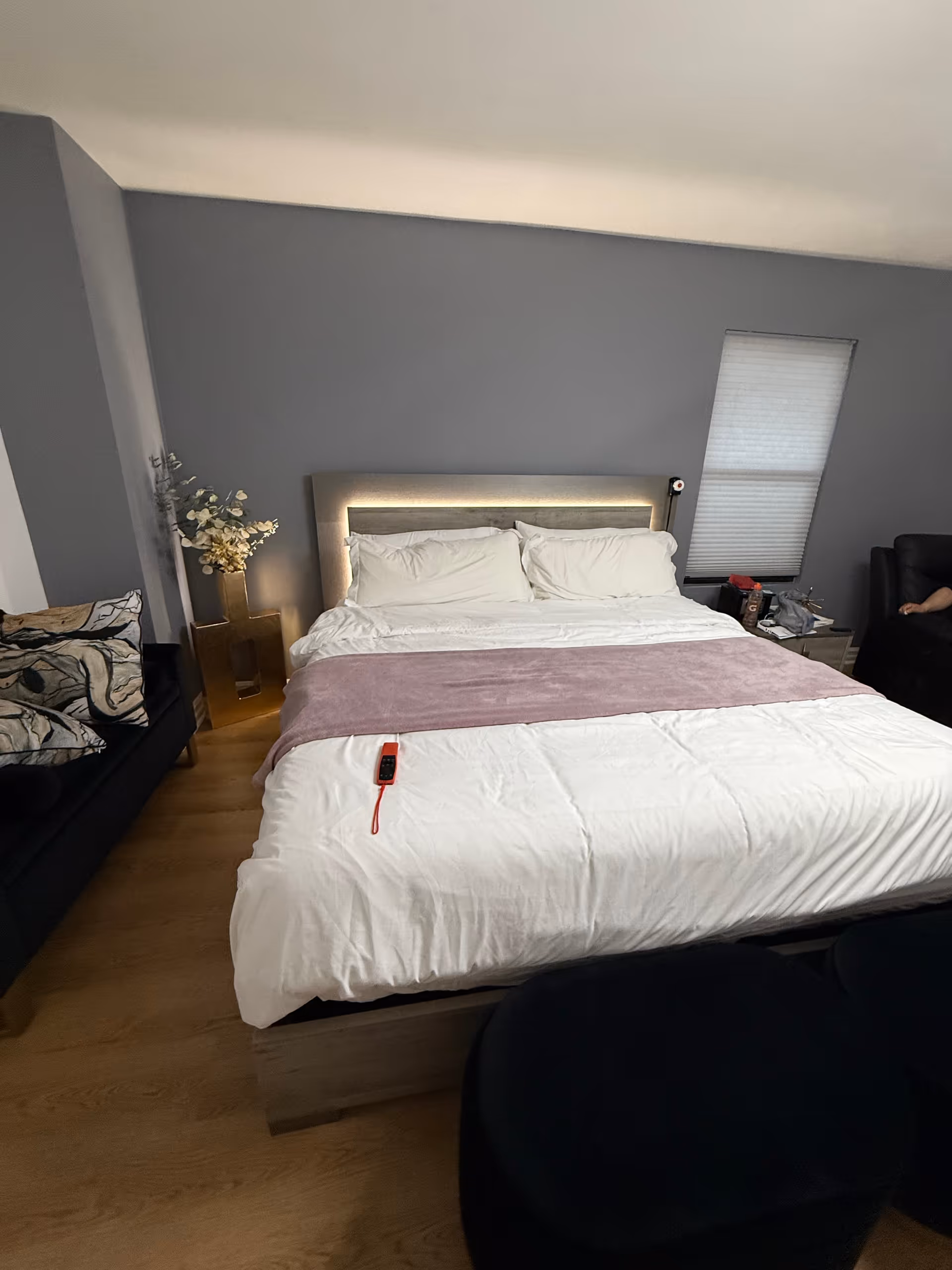 Modern bedroom with a large bed, white linens, pink throw, and gray walls.