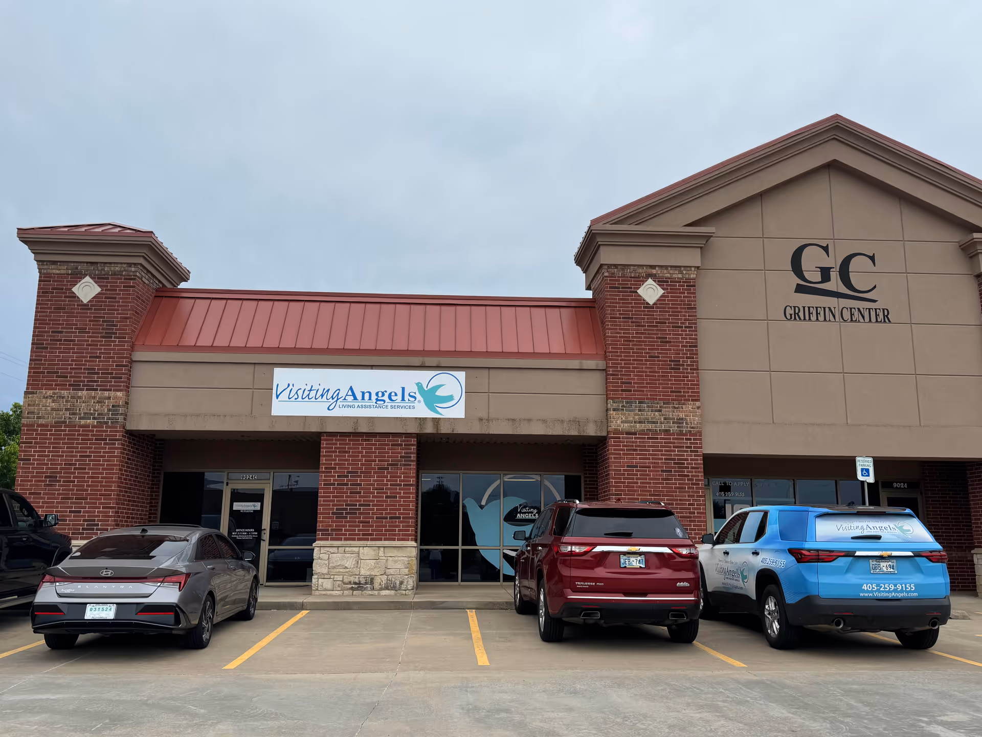 Front view of a brick building with Visiting Angels signage and parked cars.