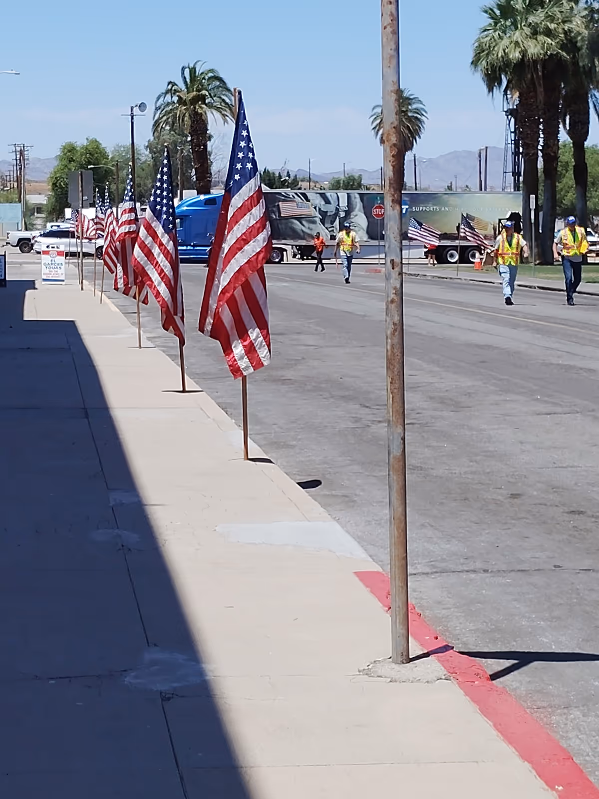 Row of American flags along a sidewalk with construction workers on a sunny street