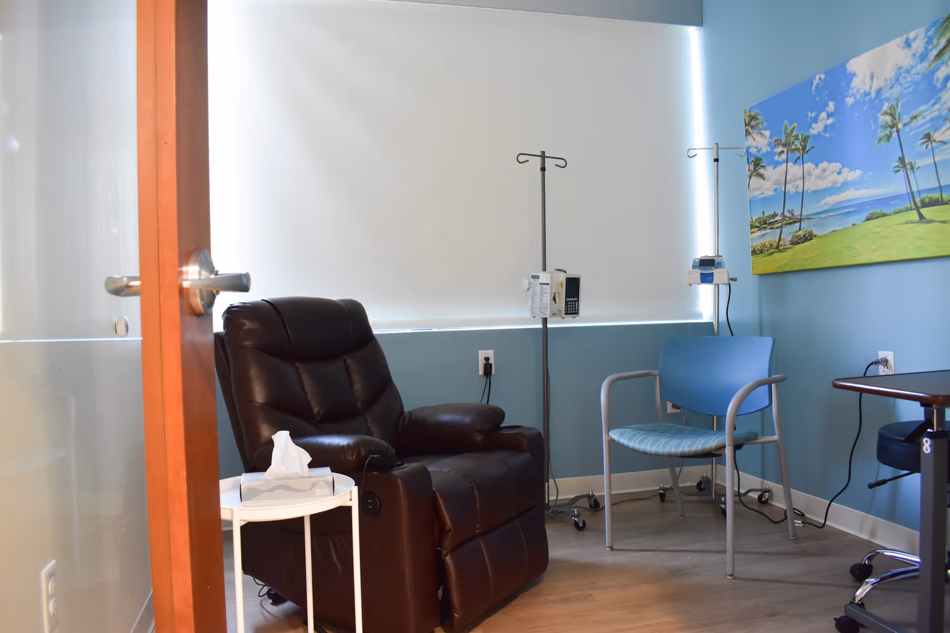 Infusion treatment room in a senior living facility with recliner chair, IV poles, and artwork.