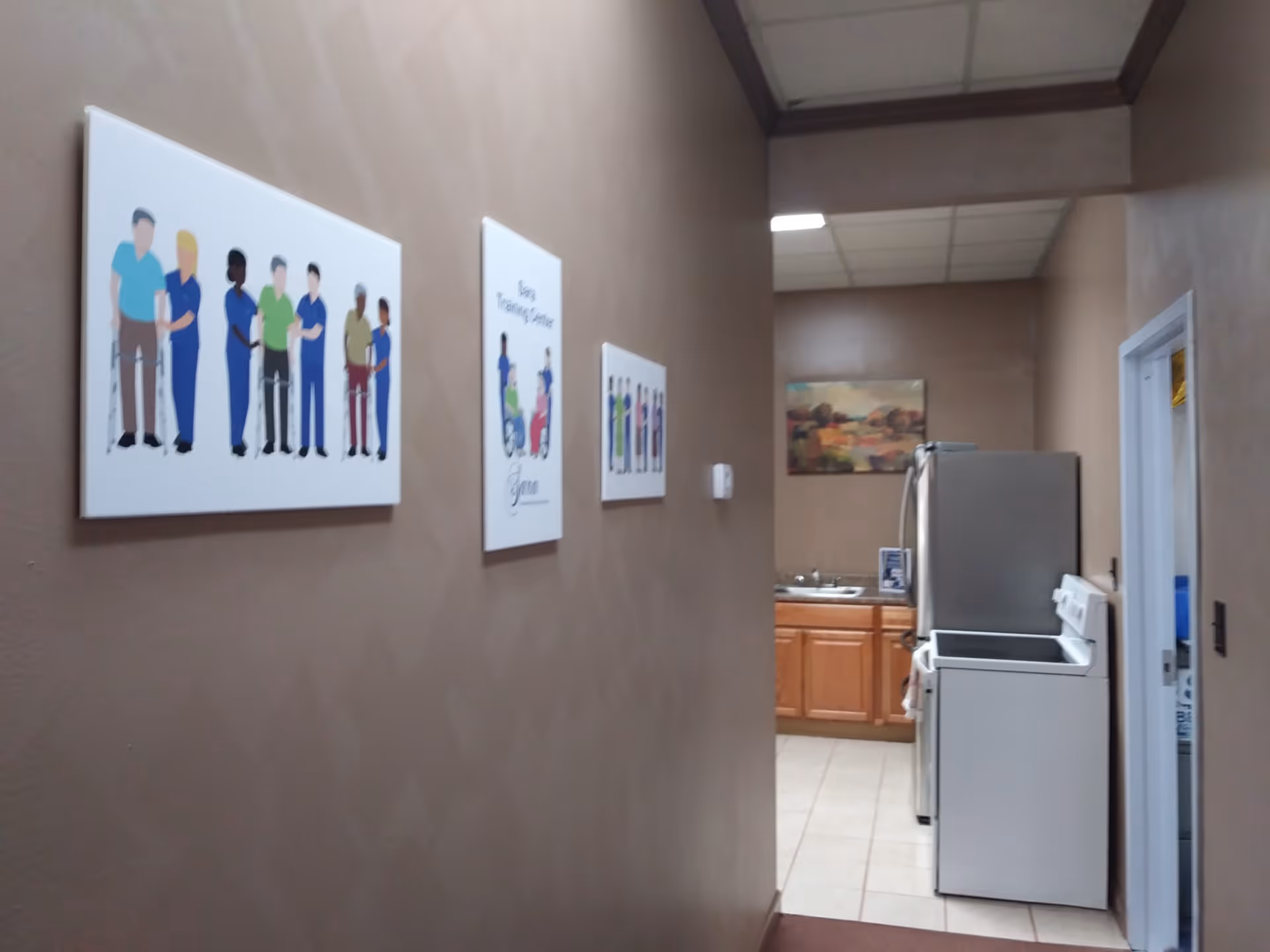 Brown hallway with wall art leads to a kitchenette with fridge and microwave.