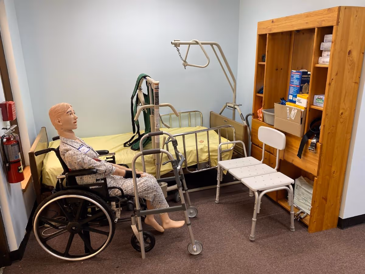 Training room with a wheelchair-bound mannequin beside a bed and medical equipment