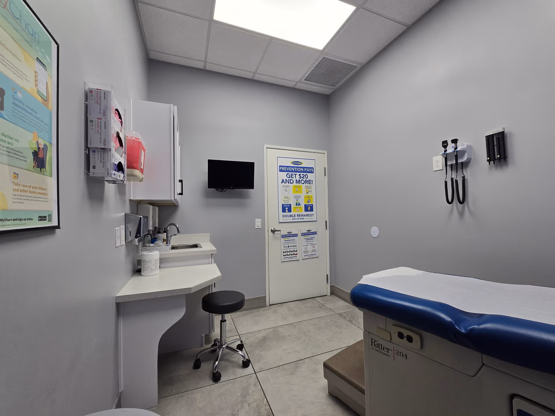 A clinical examination room with a medical bed, sink, and wall-mounted equipment.