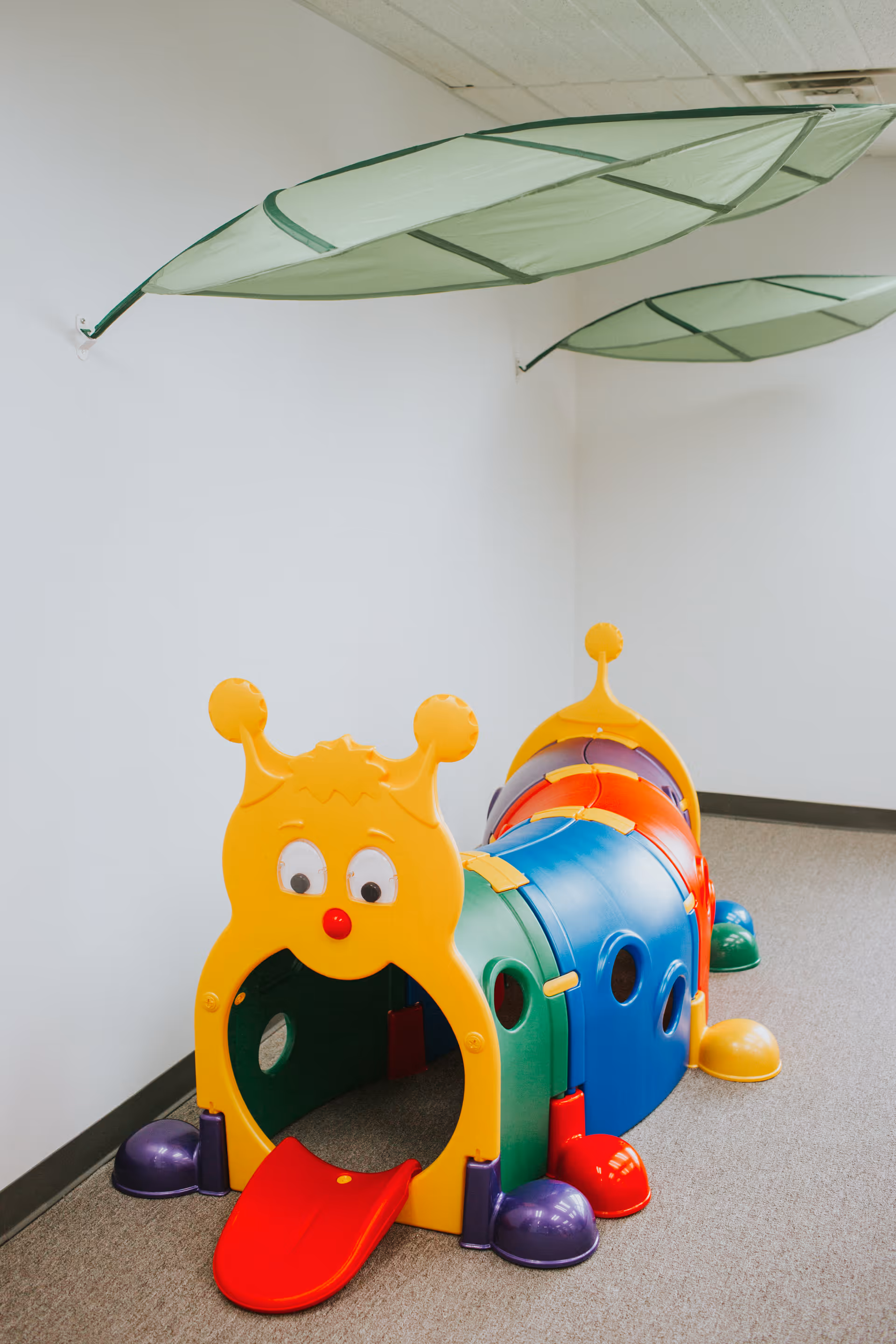 Colorful plastic play tunnel with a yellow face in a white hallway.