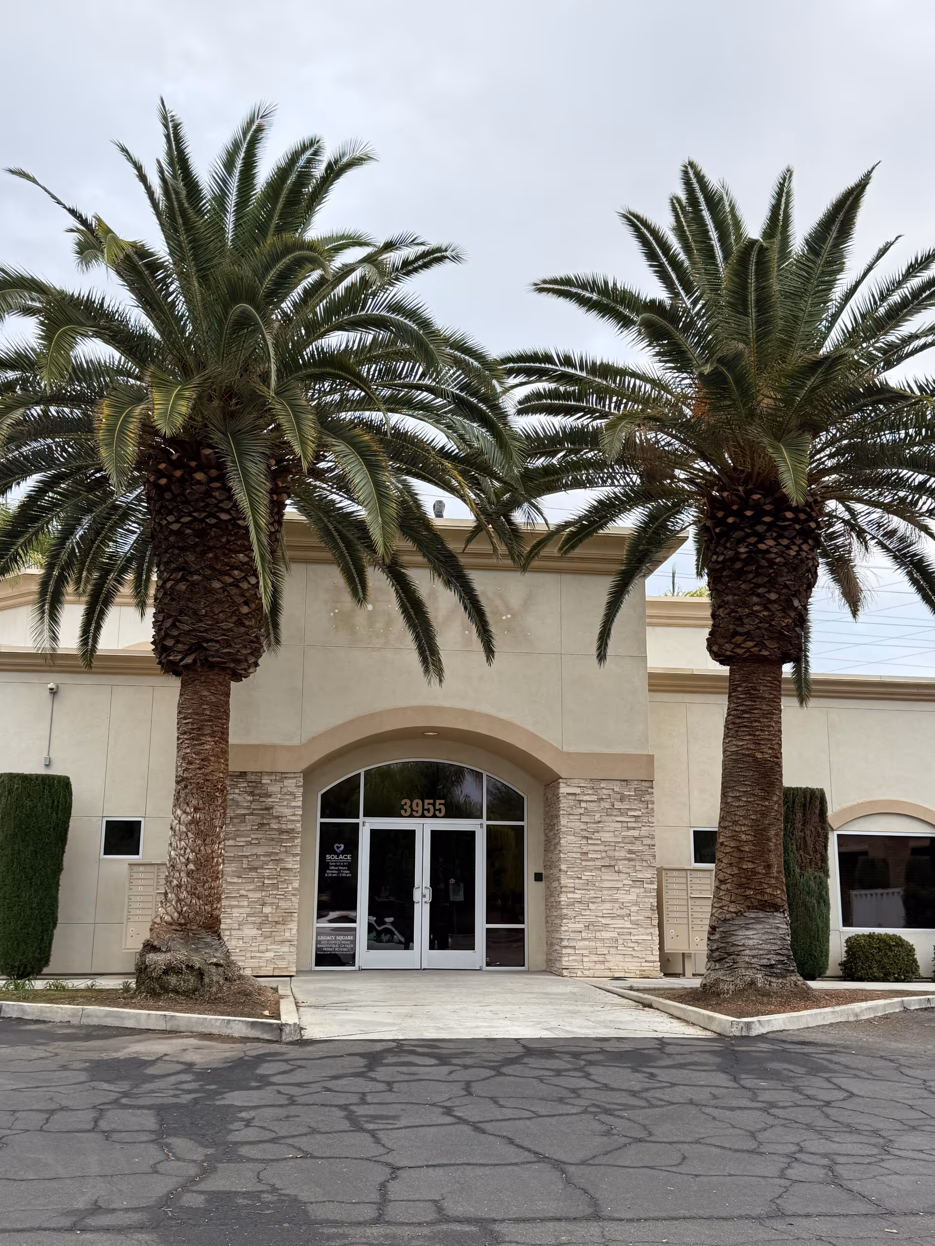 Front entrance of a beige building with two large palm trees on each side.