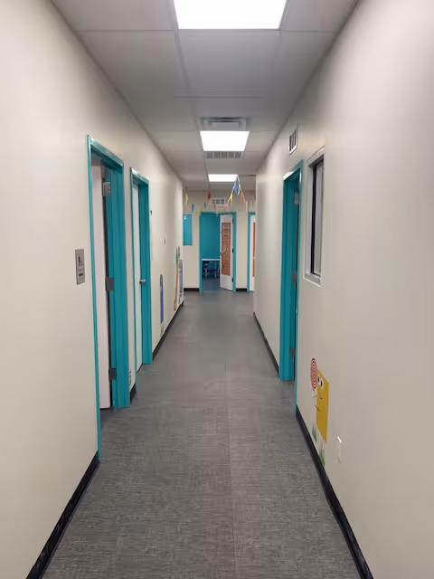 Long interior corridor with teal doors and ceiling lights in a facility hallway.