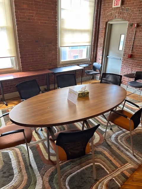 Oval wooden table with chairs in a brick-walled interior meeting room.
